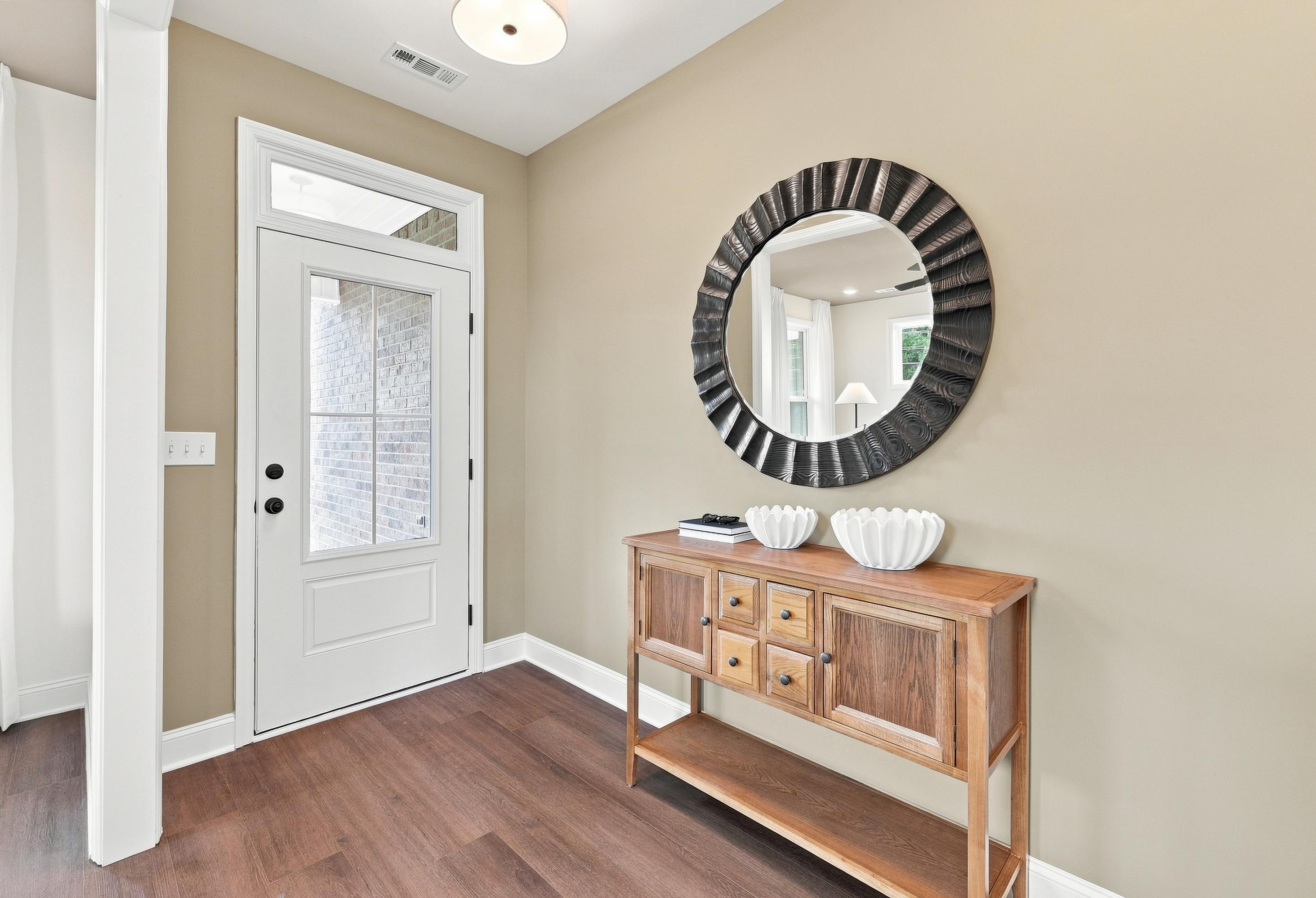 Bright entryway of The Ashport G featuring a white front door, wood console table, and round decorative mirror.
