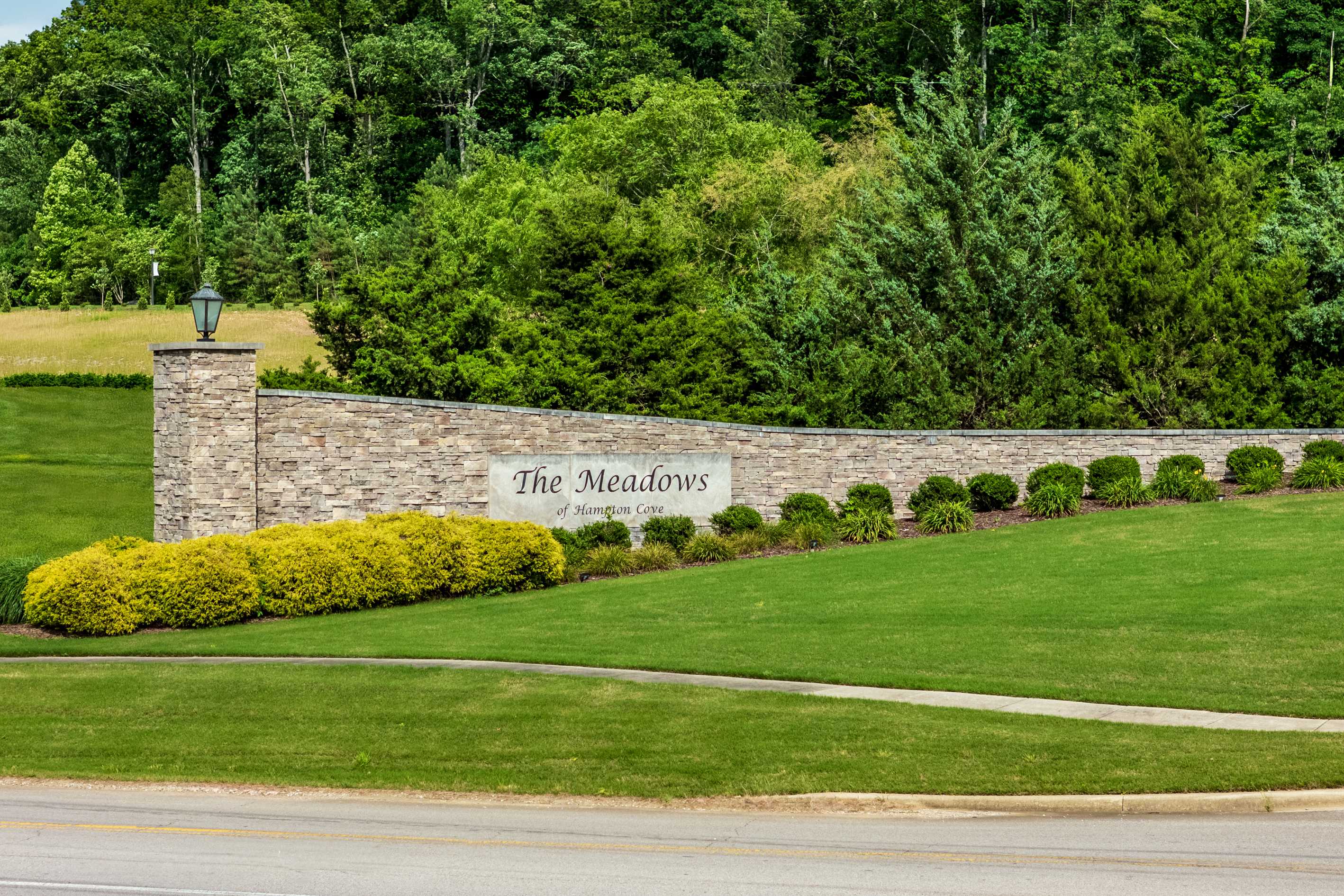 Stone entrance sign for The Meadows at Hampton Cove in Owens Cross Roads AL amid lush trees shrubs and green lawns