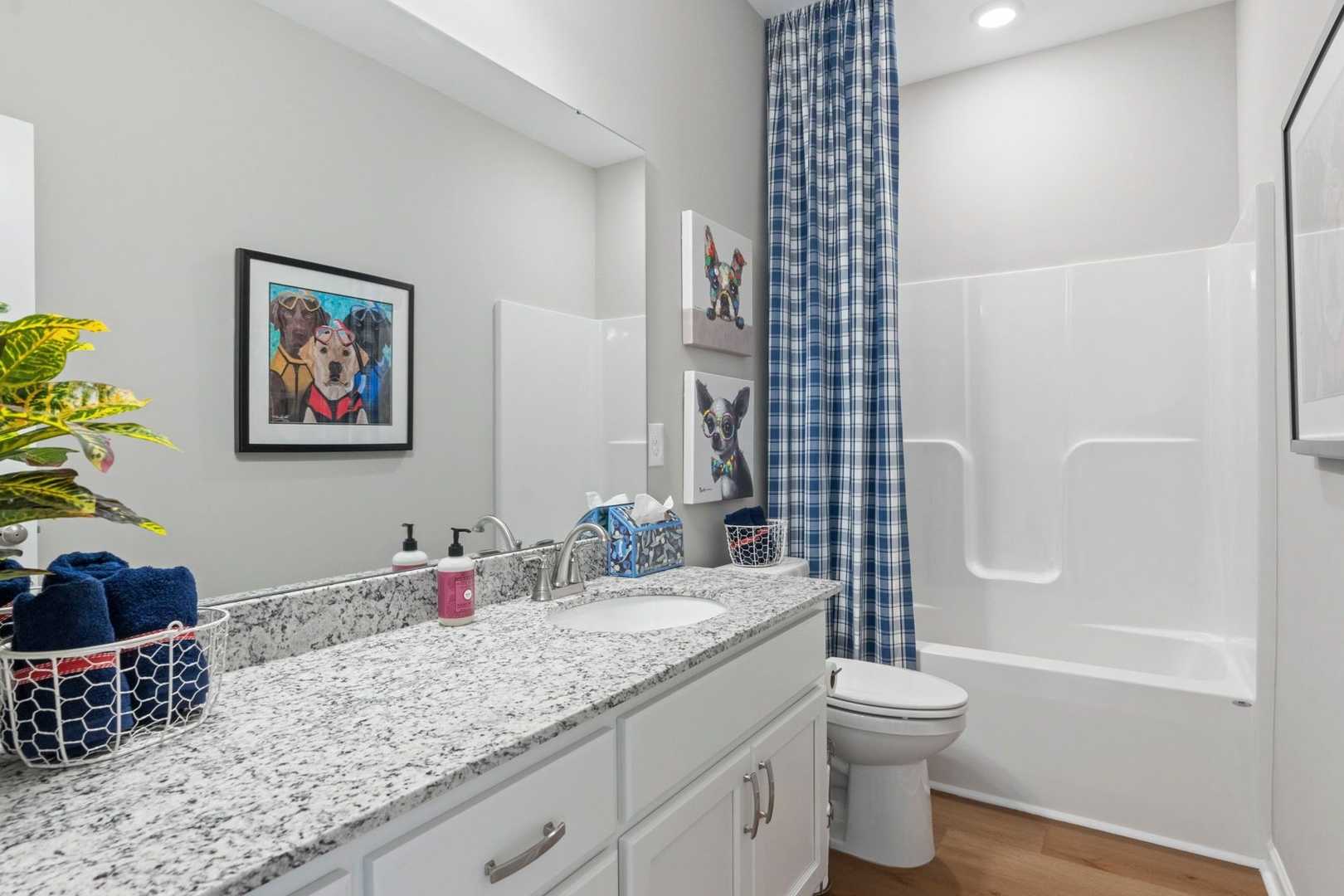 Spacious master bathroom in The Phoenix by Evermore Homes featuring granite vanity, white bathtub, and blue shower curtain