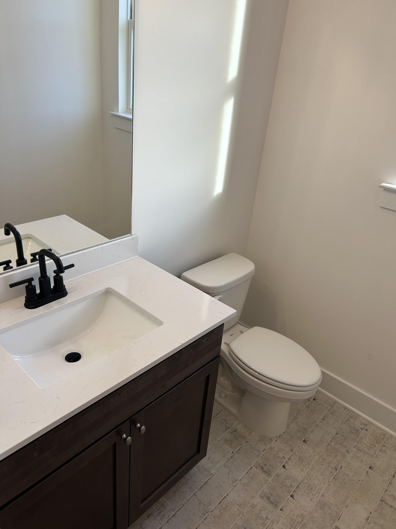 Modern powder room with white quartz vanity, dark shaker cabinets, black faucet, and toilet in Davidson Homes The Ridgeport F, Mt. Juliet, TN