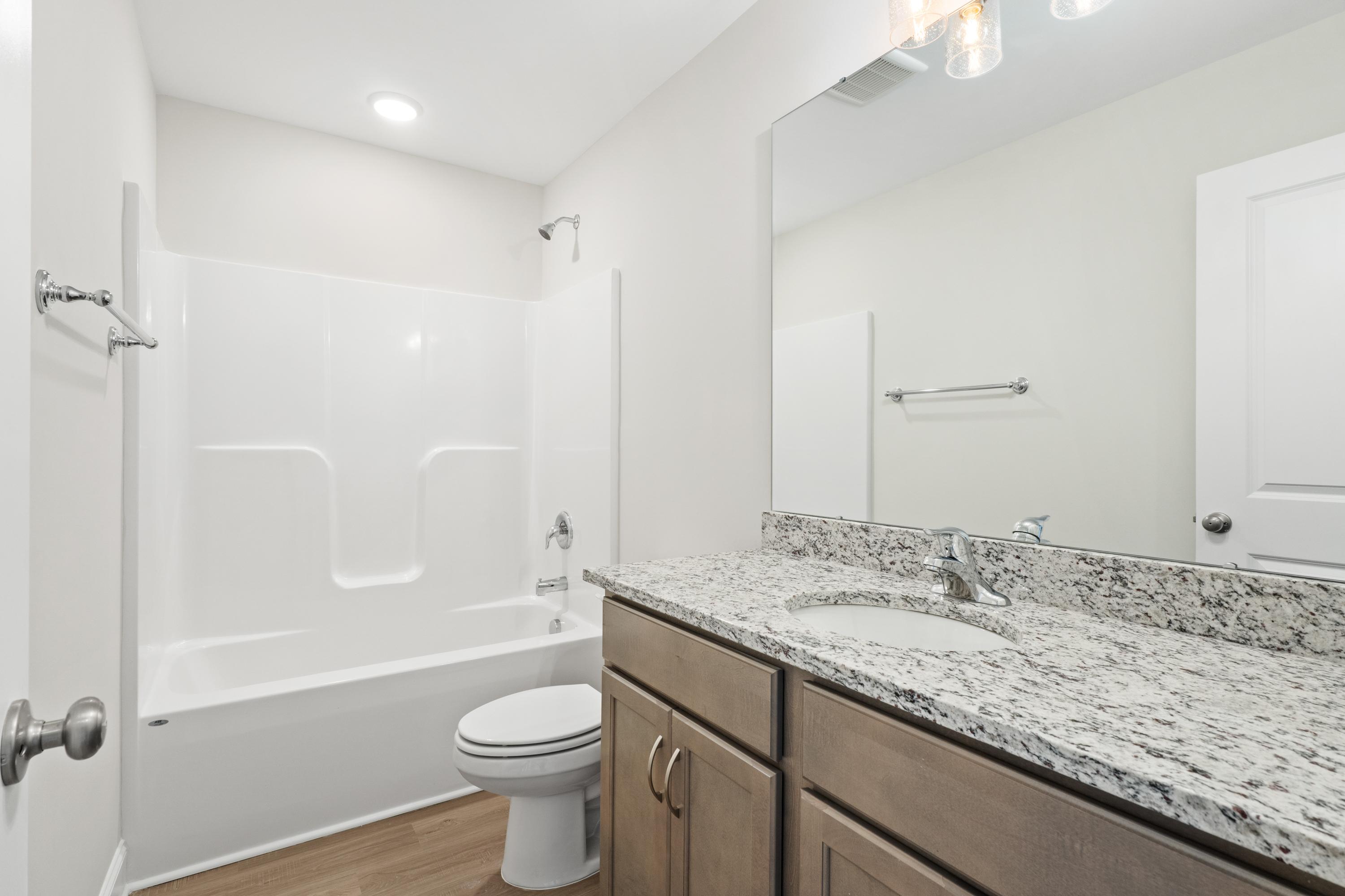 Bright secondary bathroom in The Asheville home with tub-shower combo, granite vanity, and wood flooring