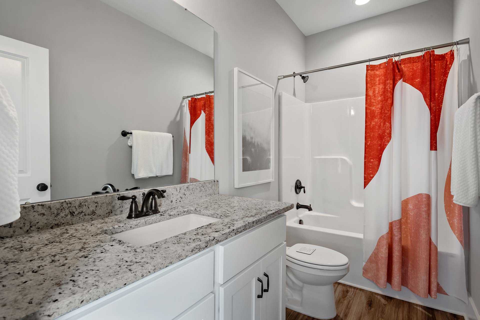 Spacious modern bathroom at Heritage Lakes in New Market Alabama with quartz vanity, red patterned shower curtain and hardwood floors