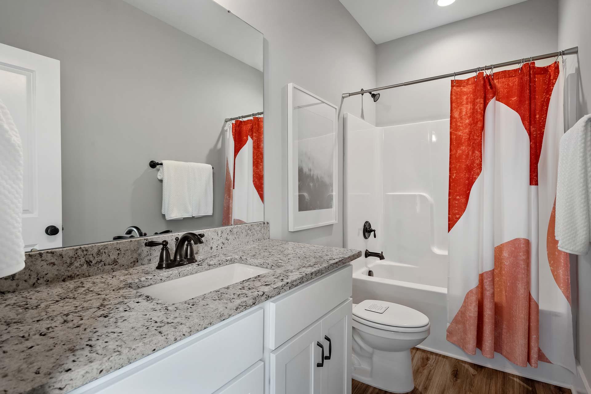 Spacious modern bathroom at Heritage Lakes in New Market Alabama with quartz vanity, red patterned shower curtain and hardwood floors