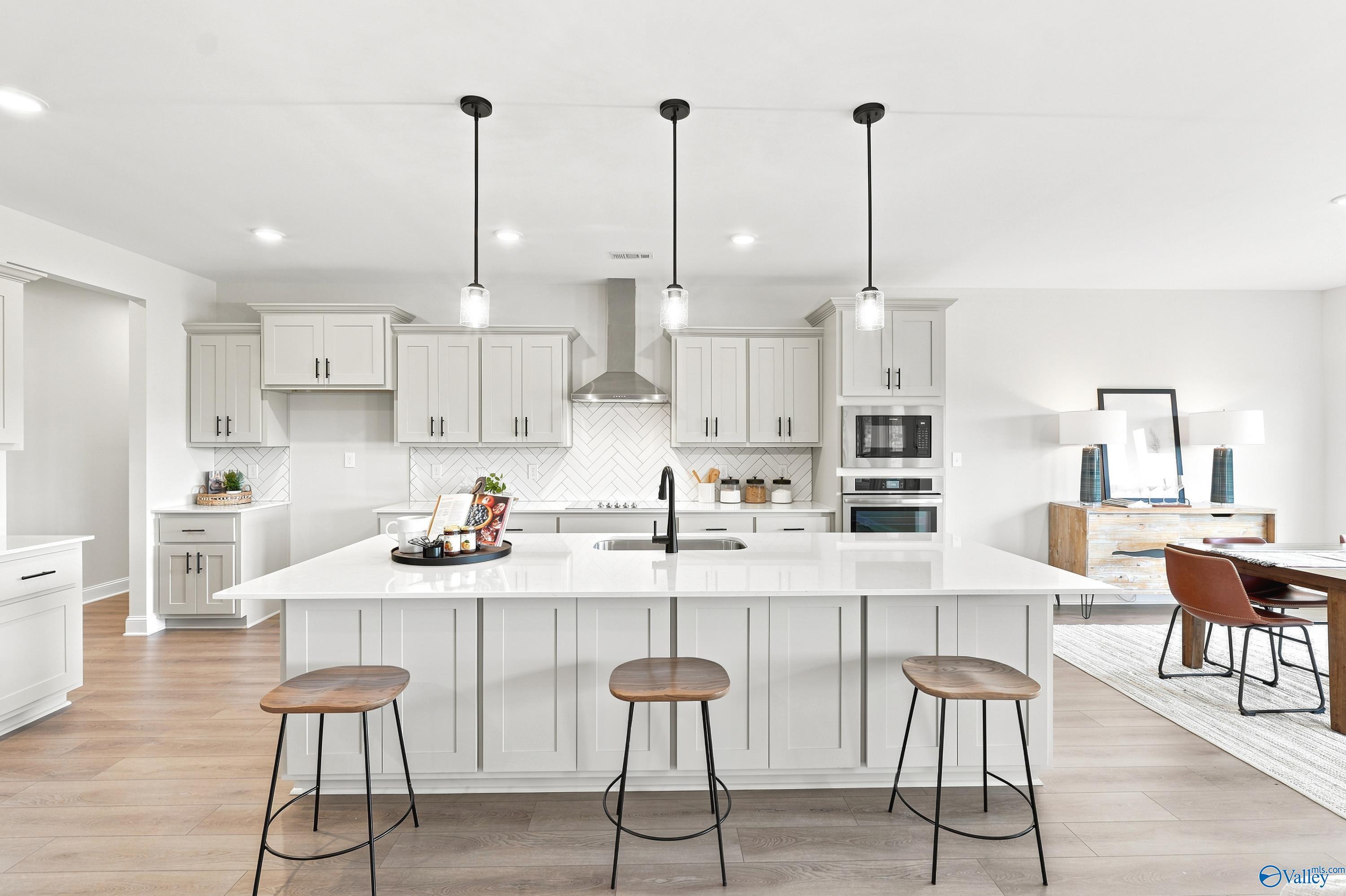 Modern kitchen with white island, pendant lighting, and herringbone backsplash in The Finleigh, Riverton Preserve, Huntsville.
