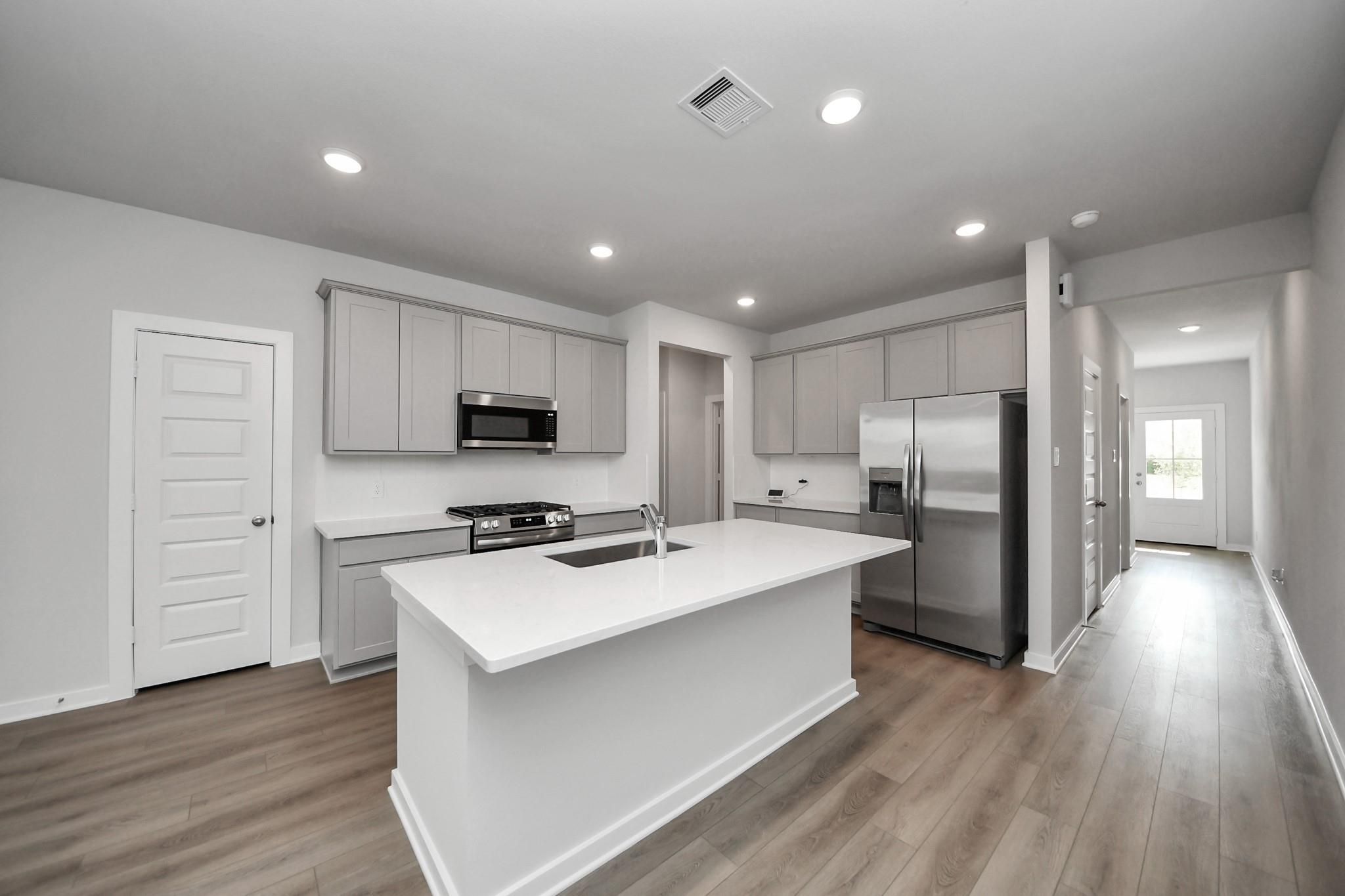Modern kitchen with island, quartz countertops, and stainless appliances in The Frio F plan at Robins Landing, Houston.