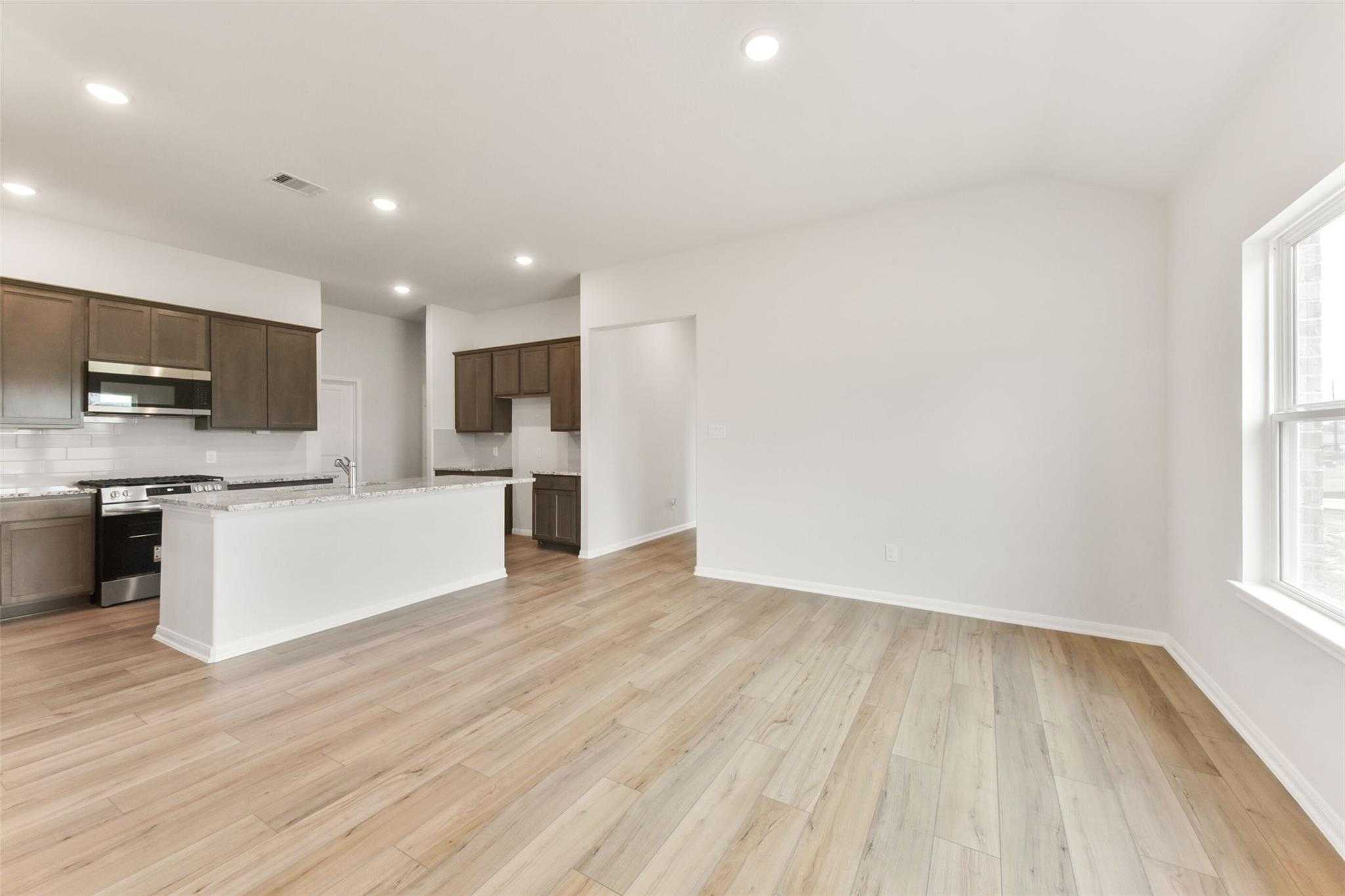Open-concept kitchen with brown shaker cabinets, white quartz island, stainless appliances, and light oak floors in The Laguna B, Magnolia, Texas