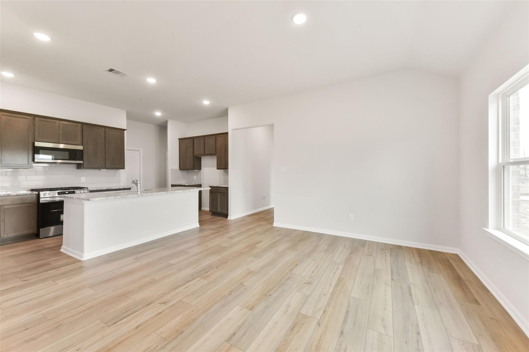 Open-concept kitchen with brown shaker cabinets, white quartz island, stainless appliances, and light oak floors in The Laguna B, Magnolia, Texas