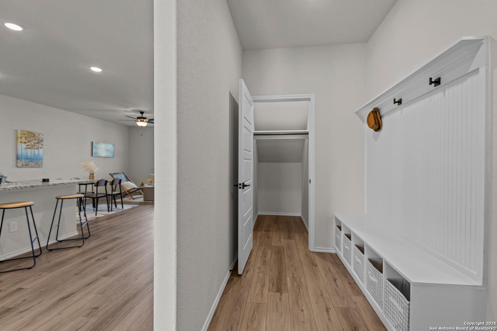 White mudroom with built-in coat rack, bench, and shelves overlooking open kitchen in Davidson Homes The Douglas C, Seguin, TX