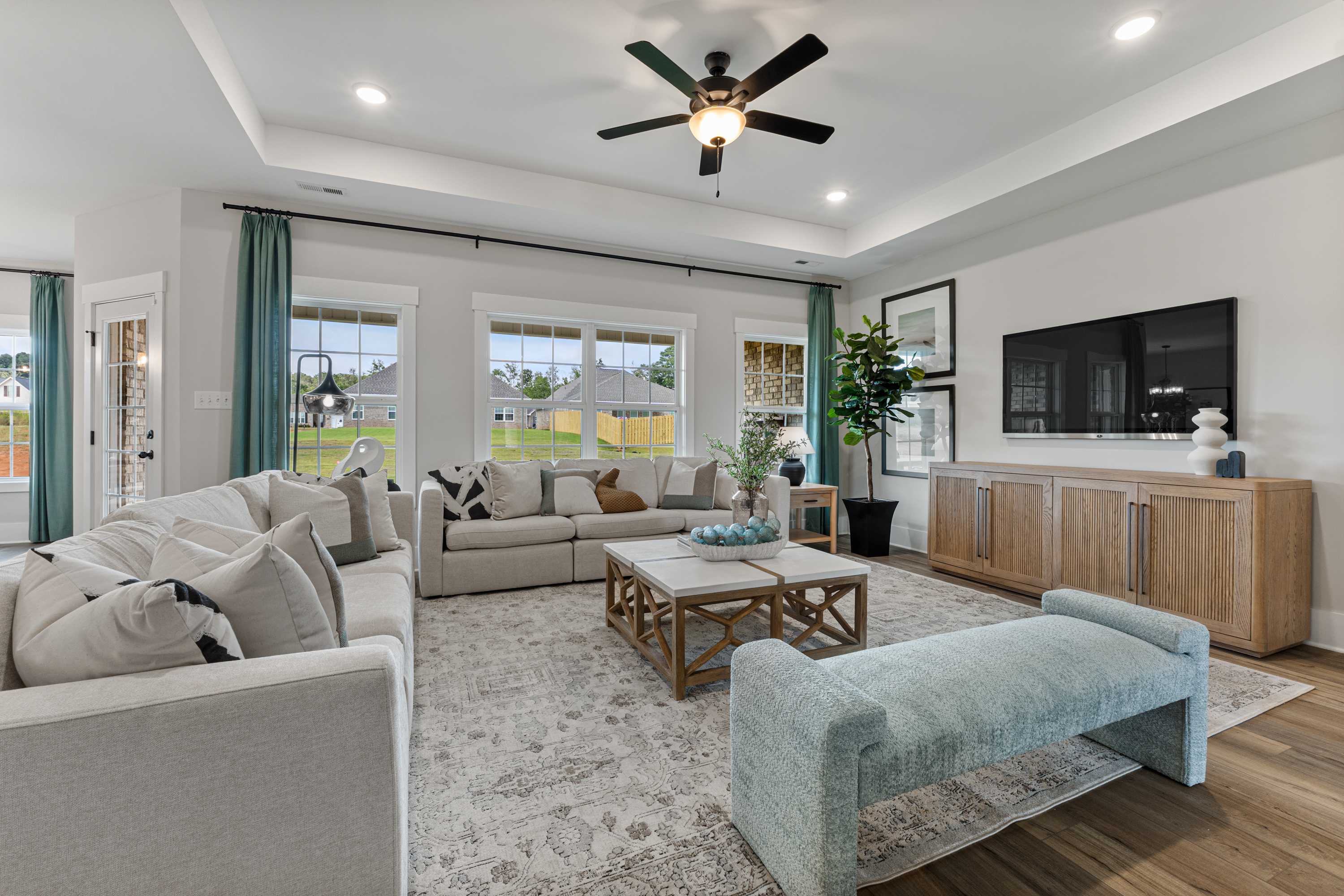 Open-concept living room at River Road Estates in Decatur AL with beige sectional sofa, hardwood floors, large windows, and ceiling fan