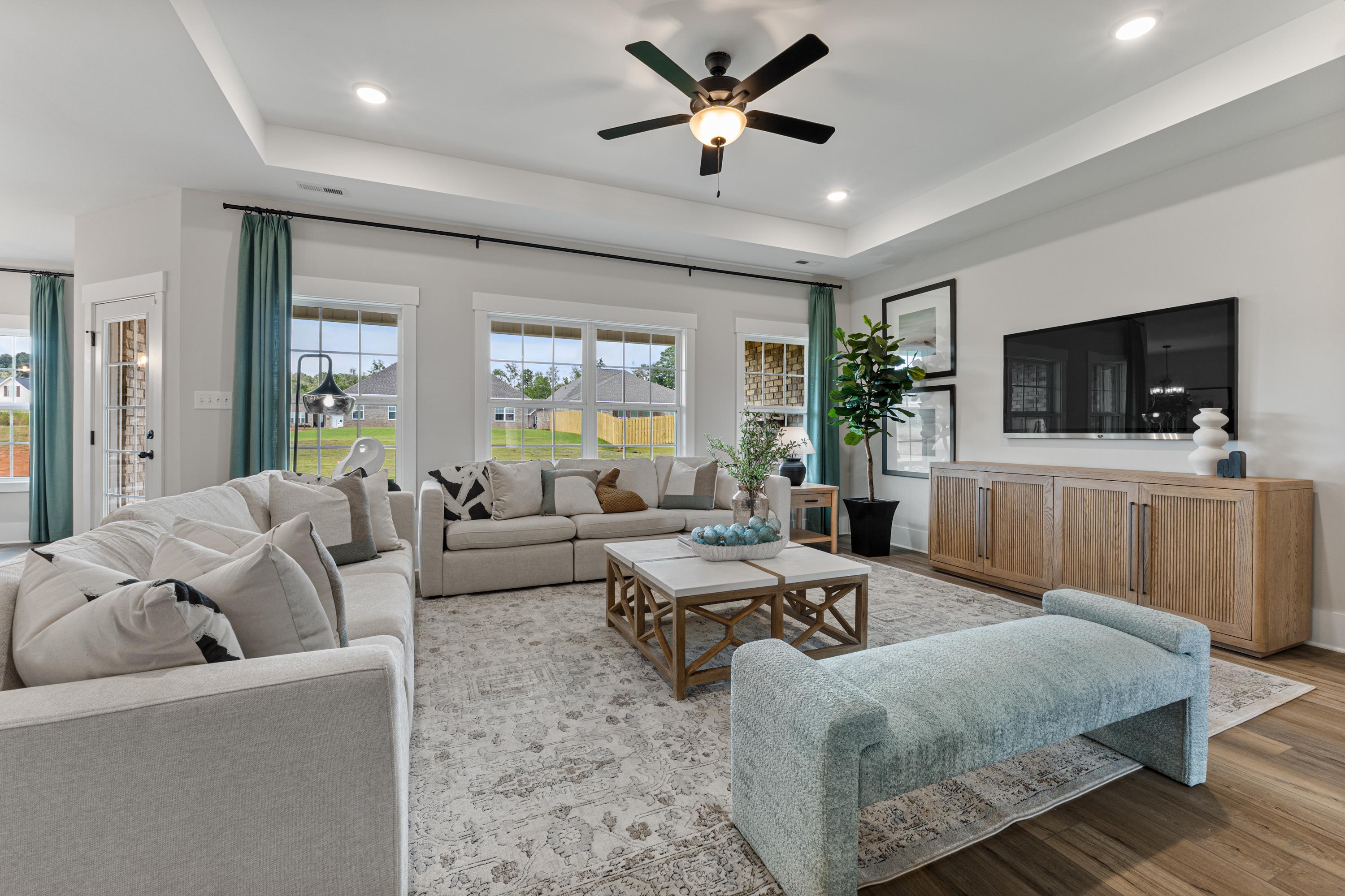 Open-concept living room at River Road Estates in Decatur AL with beige sectional sofa, hardwood floors, large windows, and ceiling fan