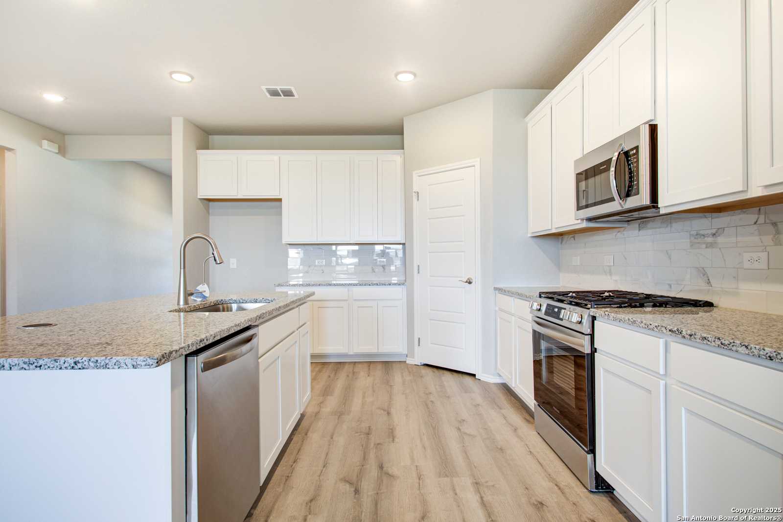 Bright modern kitchen with white cabinets, granite countertops, stainless steel appliances, and large island in Davidson Homes The Douglas G, San Antonio