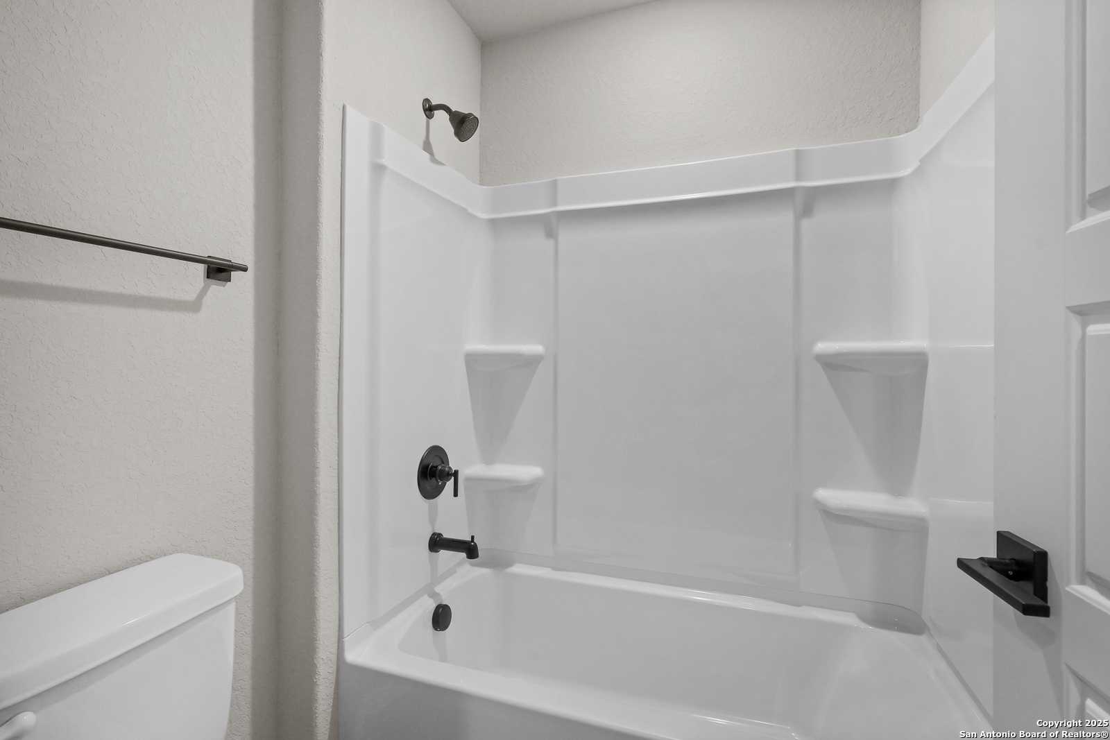 Modern white bathroom with glass shower, deep soaking tub, black fixtures in Davidson Homes The Charlotte B, San Antonio
