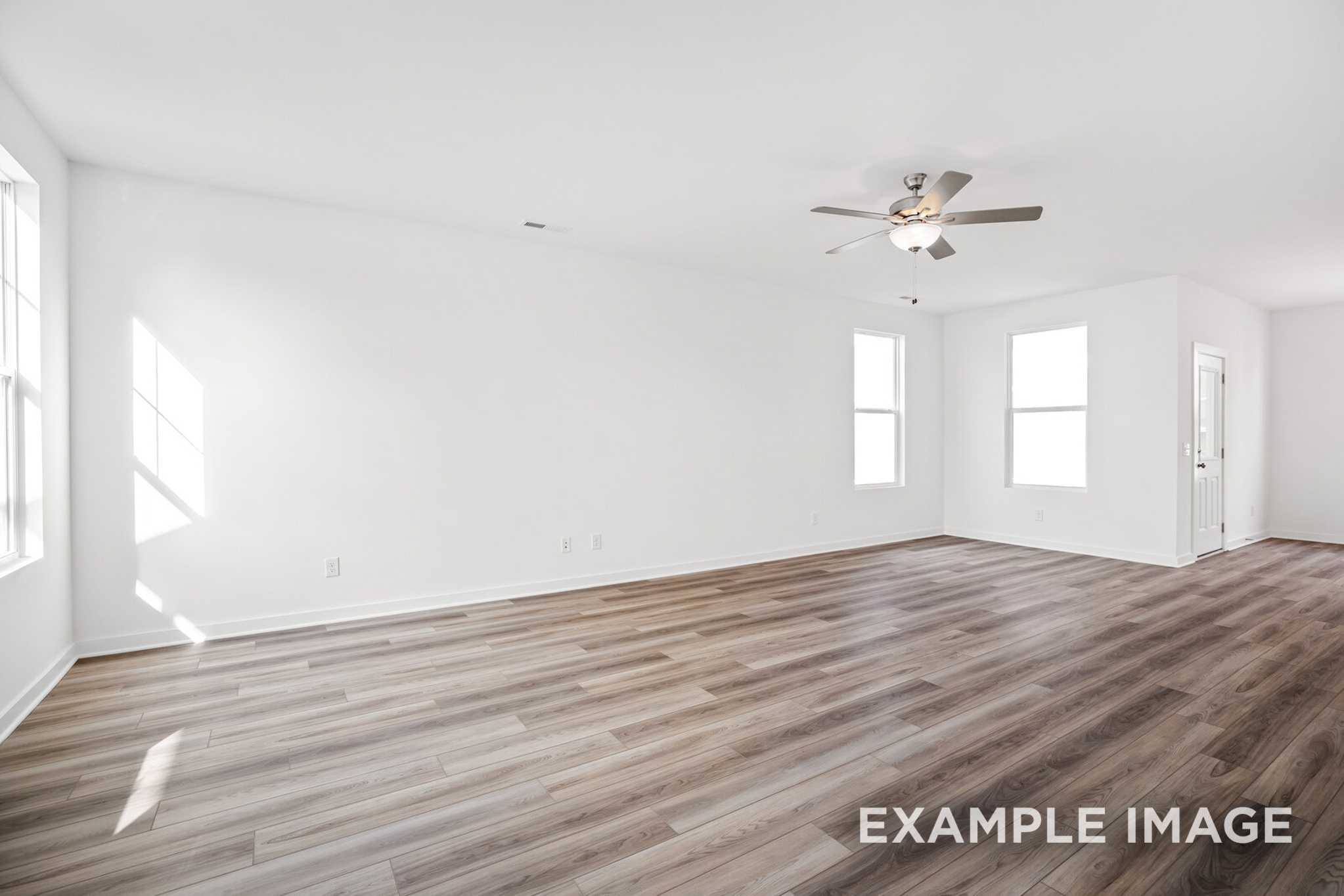 Spacious empty living room in The Murray B showcasing white walls, large windows, sunlight, ceiling fan, and hardwood floors