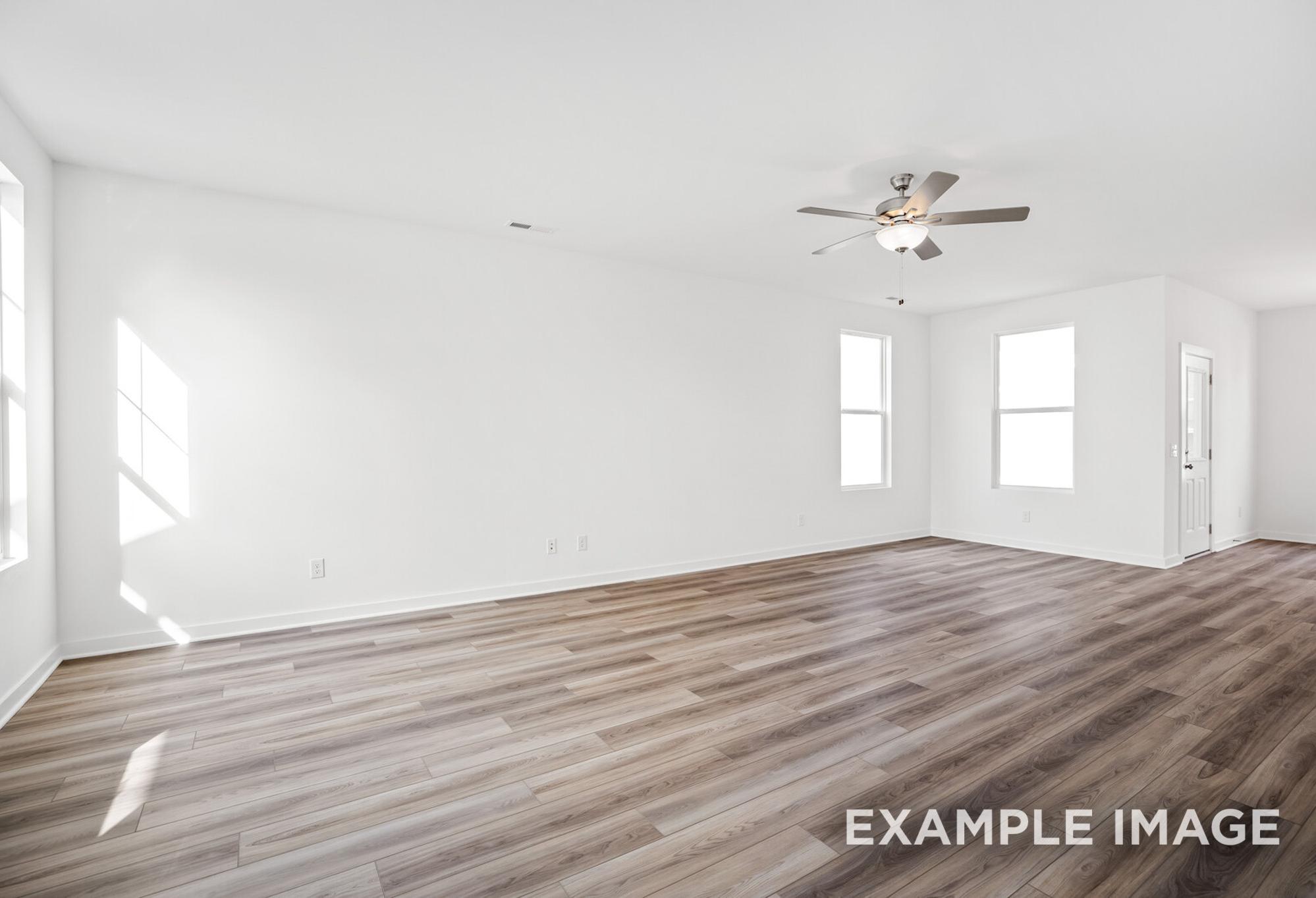 Spacious empty living room in The Murray B showcasing white walls, large windows, sunlight, ceiling fan, and hardwood floors