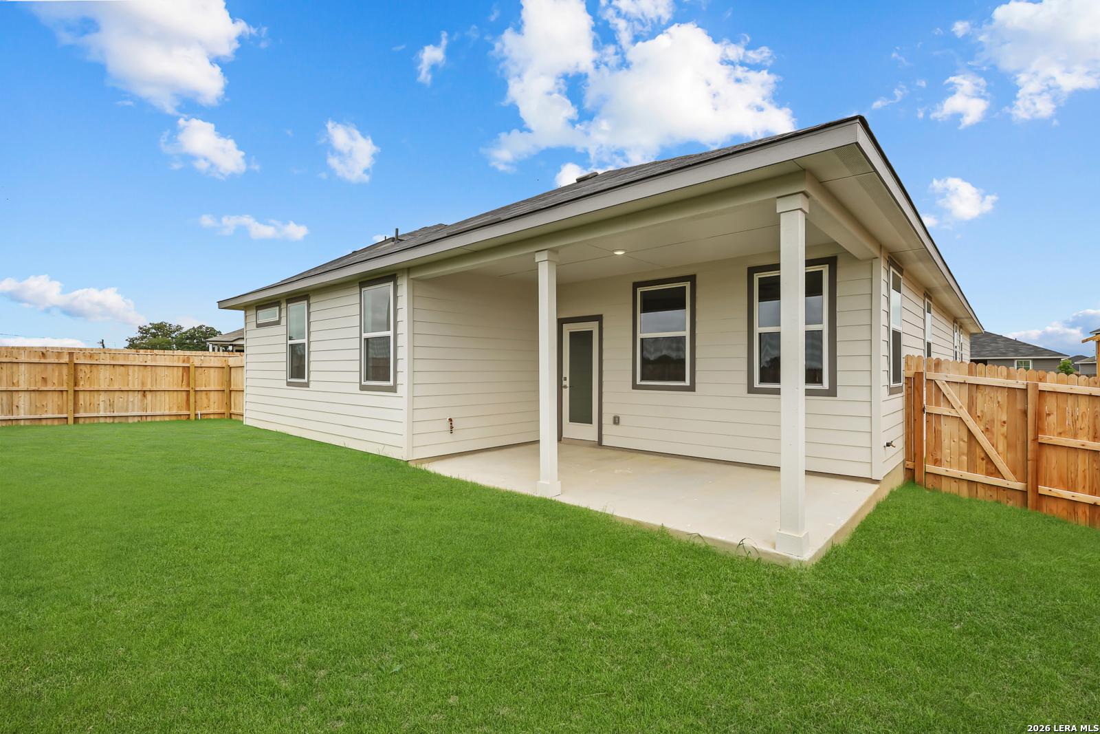 Covered patio with columns on beige single-story home, lush green backyard, wooden fence in Hickory Ridge, Elmendorf, Texas