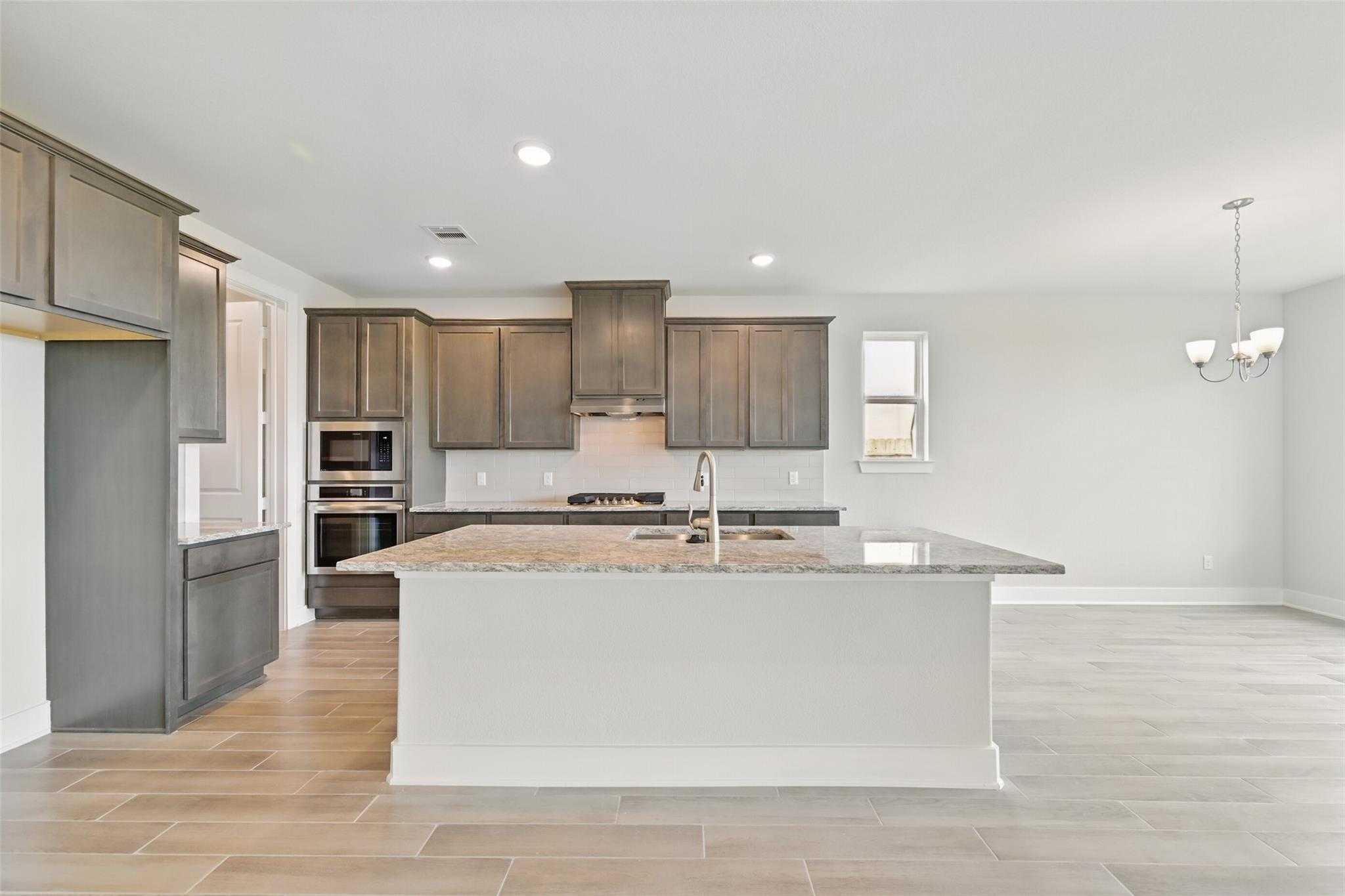 Modern kitchen featuring gray shaker cabinets, granite island with sink, stainless double ovens in Davidson Homes The Philip A, Texas City