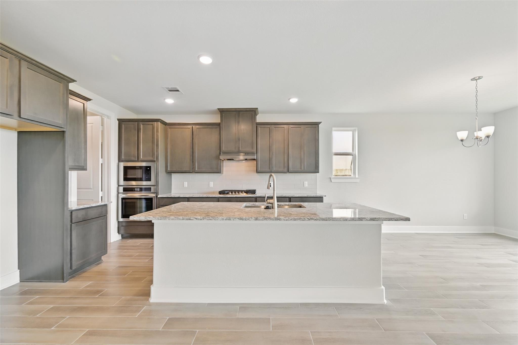 Modern kitchen with gray shaker cabinets, granite island sink, stainless double ovens in Davidson Homes The Philip A, Texas City