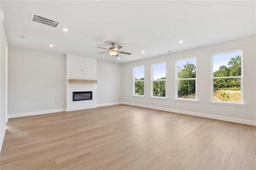 Bright family room with white brick gas fireplace, ceiling fan, light wood floors, and large windows overlooking lush greenery in Davidson Homes The Hampton C, Buford, GA