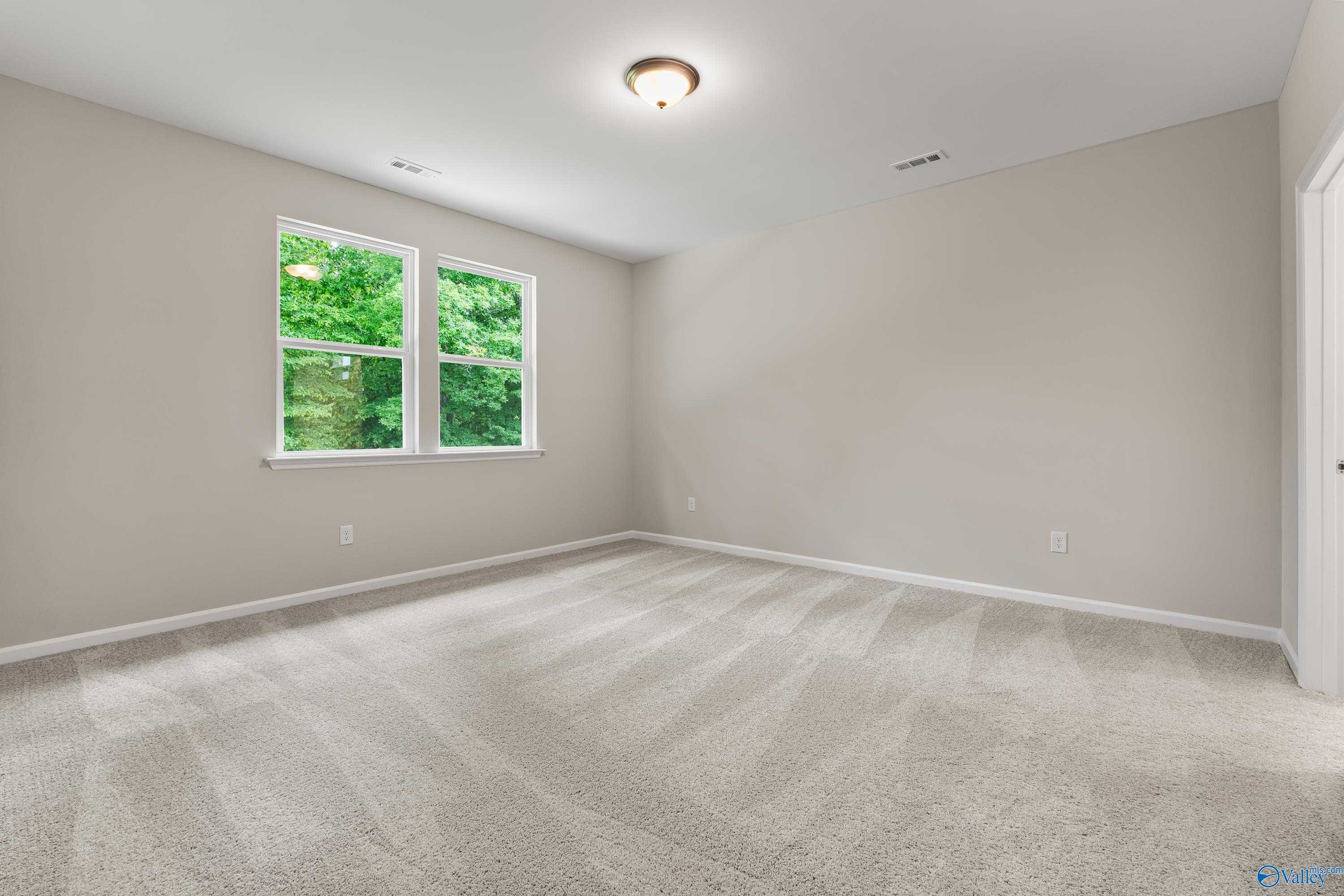 Spacious empty bedroom with beige walls, carpet floor, large windows to greenery in The Phoenix 3-bedroom home, Fayetteville, TN