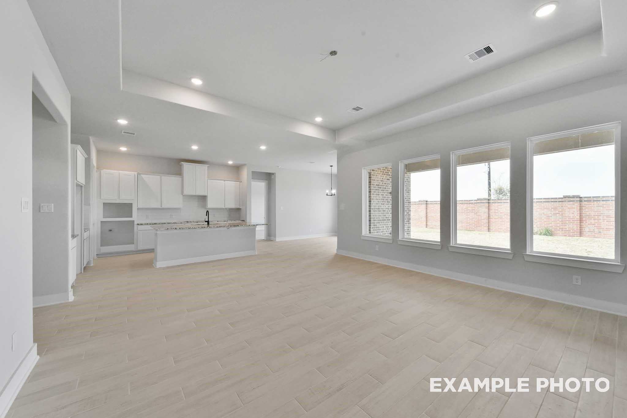 Open-concept kitchen-living area with white cabinets, granite island, large windows to backyard in Davidson Homes The George A, Texas City