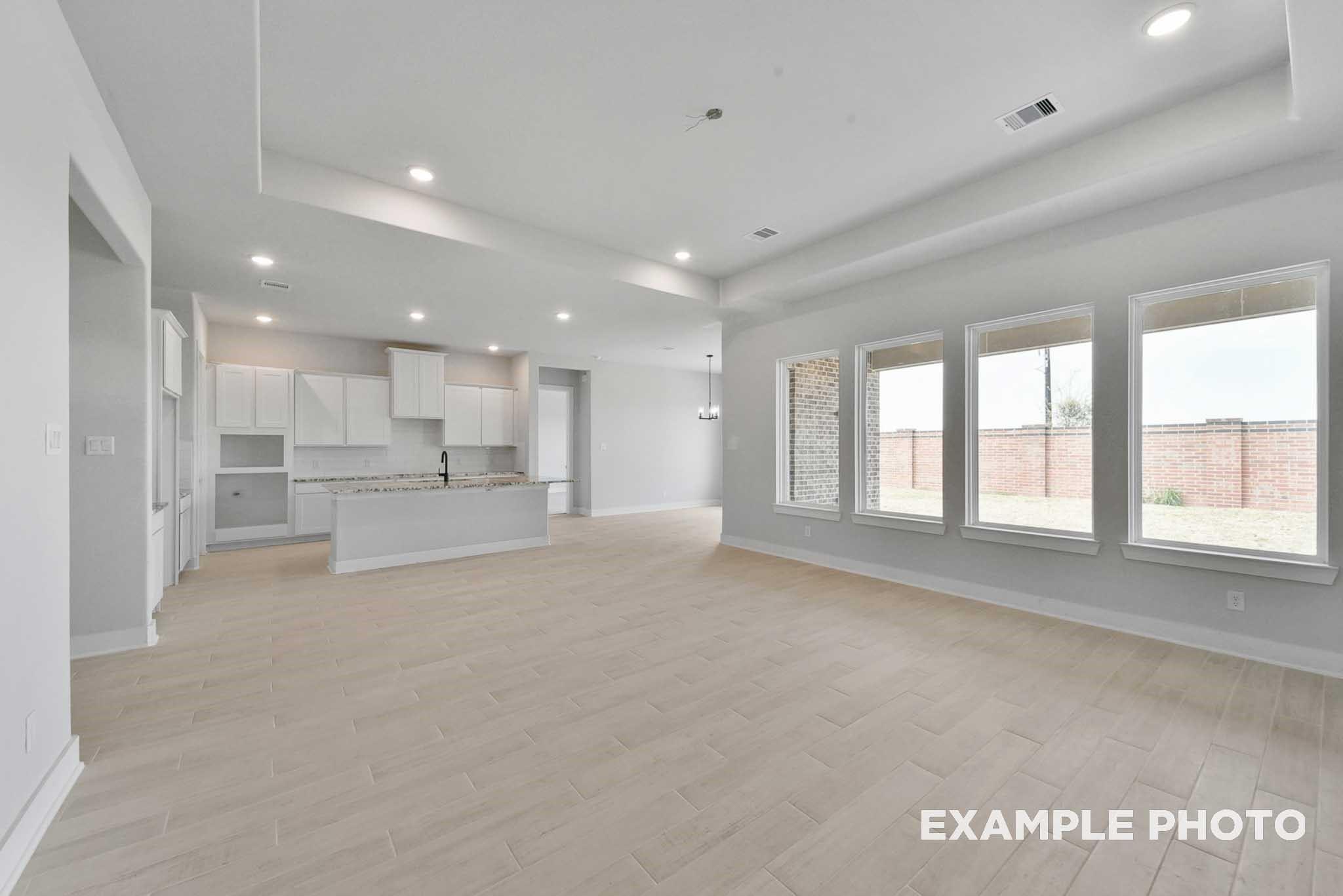 Spacious open-concept kitchen and living area with white cabinets, island, and large windows overlooking backyard in Davidson Homes The George A, Texas City