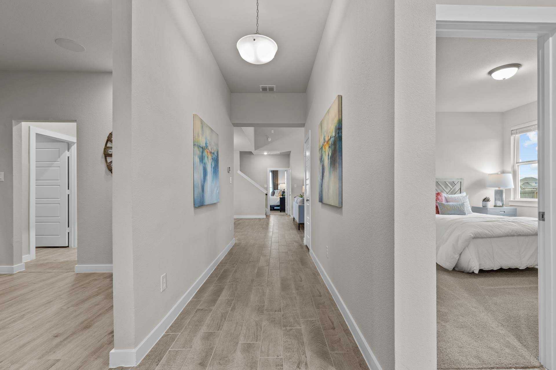 Spacious hallway in The Collin B home with light wood floors, abstract art, and master suite entry, Seguin Texas