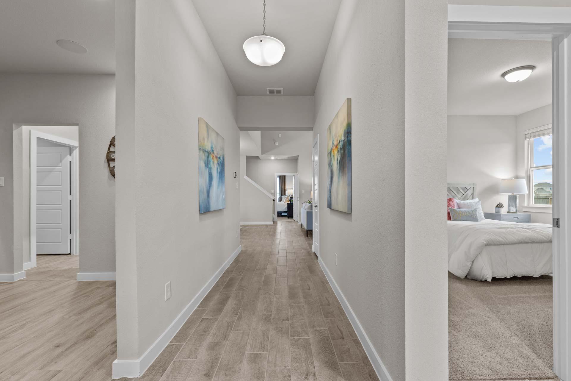 Spacious gray hallway with hardwood floors, abstract wall art, and open doorway to airy master bedroom in The Collin A, Seguin TX
