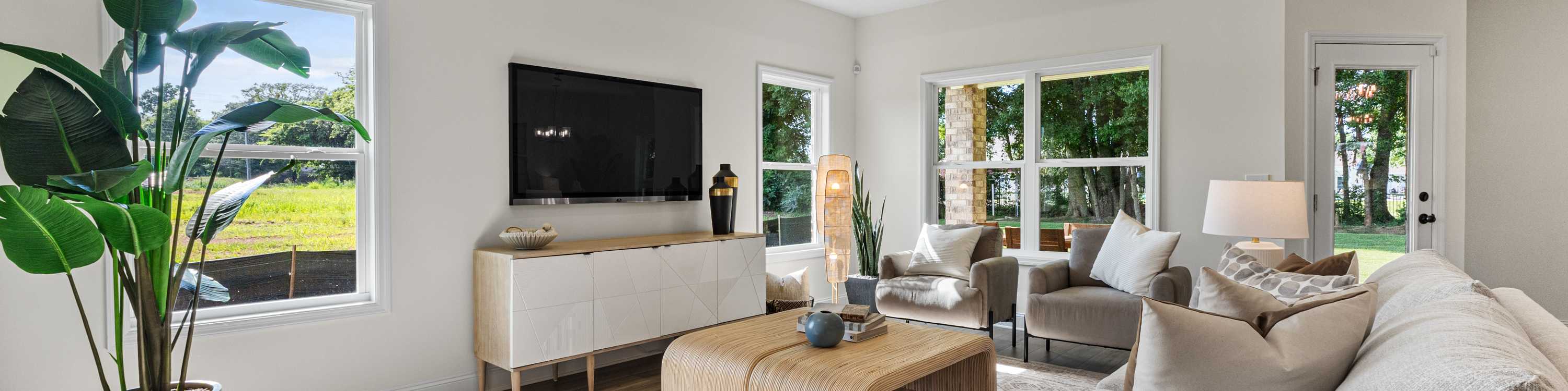 Spacious living room at Little Creek in Arab Alabama with large windows, beige sofa, ceiling fan, tropical plants