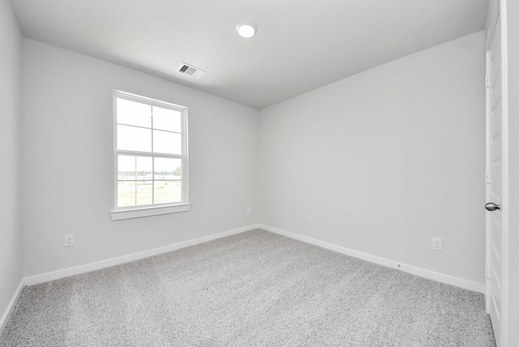 Bright, carpeted bedroom with neutral walls in The Blanco F floor plan at Spring Branch Crossing, Conroe, Texas.