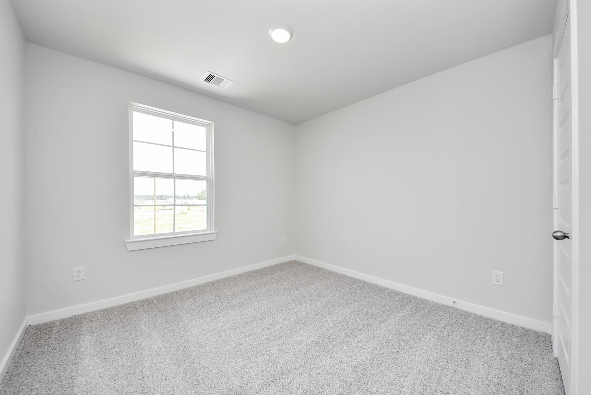 Bright, carpeted bedroom with neutral walls in The Blanco F floor plan at Spring Branch Crossing, Conroe, Texas.