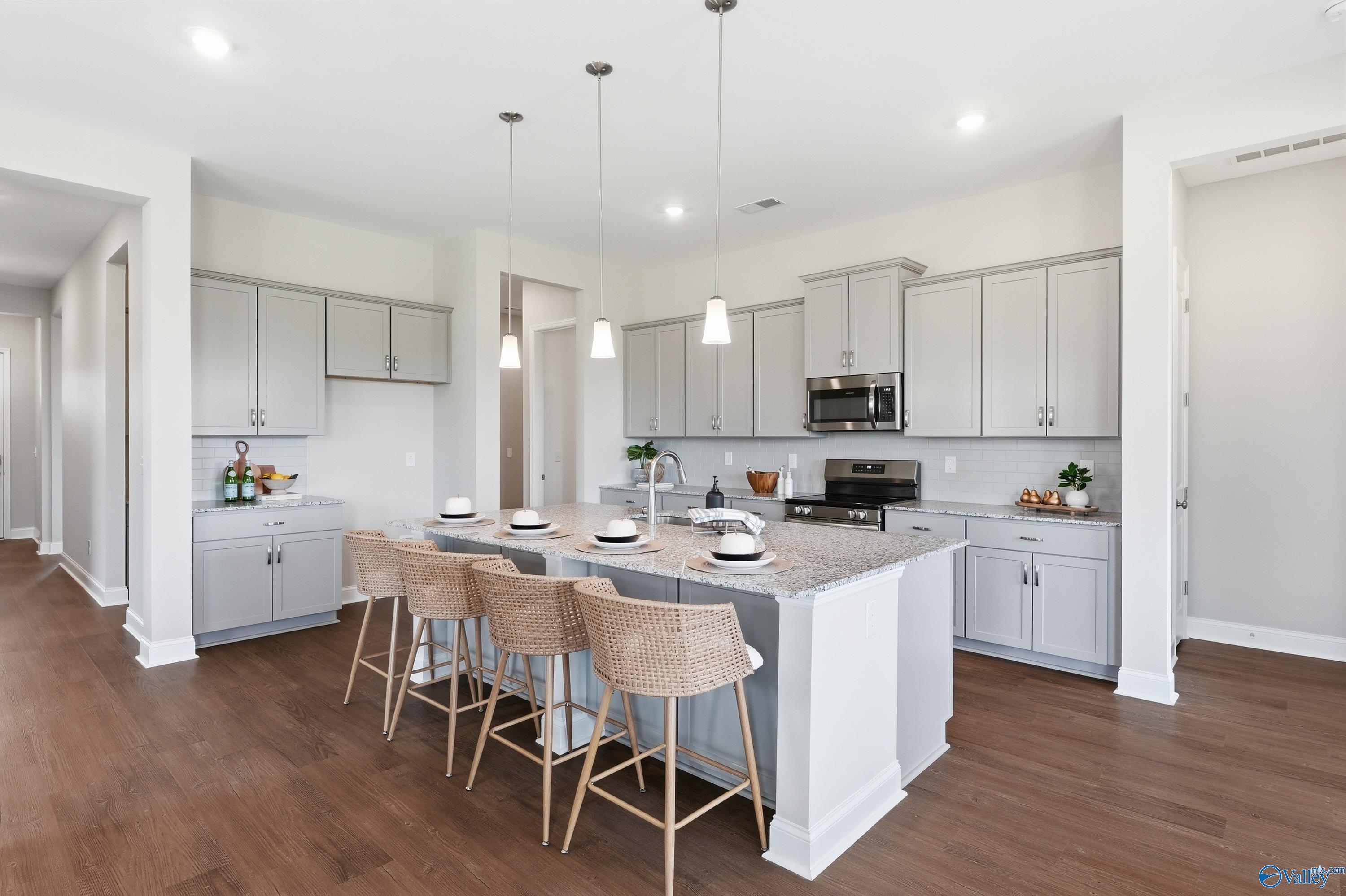 Modern kitchen featuring gray shaker cabinets, quartz island with pendant lights, stainless appliances in Davidson Homes The Arcadia B, Huntsville AL