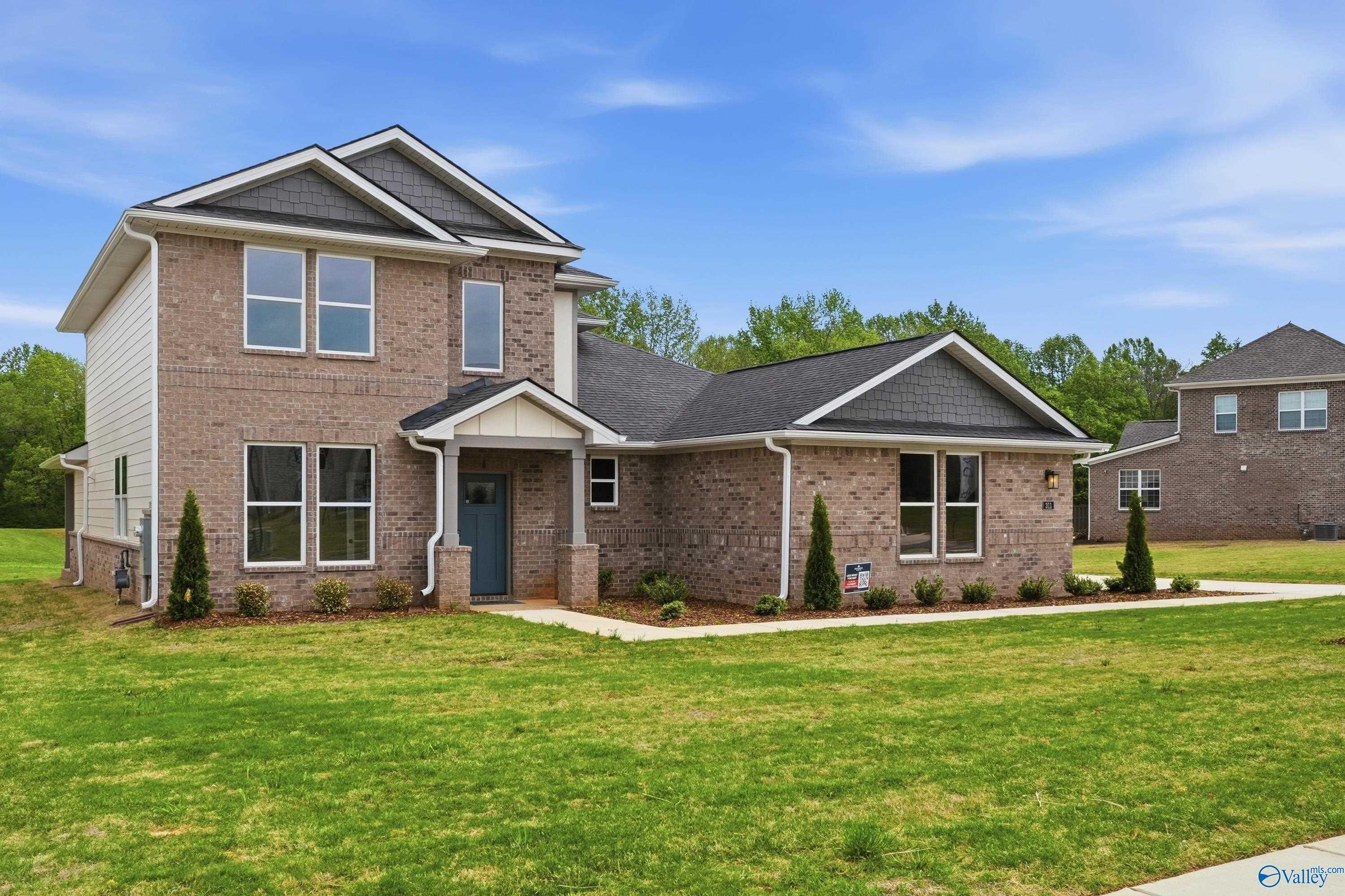 Two-story brick and siding home with blue door, evergreens, shrubs, and lush green lawn in Riverton Preserve, Huntsville, Alabama - Davidson Homes Dorado