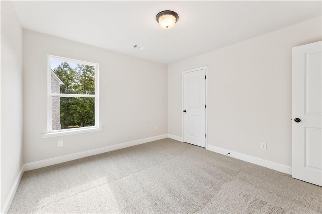 Bright secondary bedroom with large window overlooking trees, white walls, and carpet in Davidson Homes The Hickory B, Buford, GA