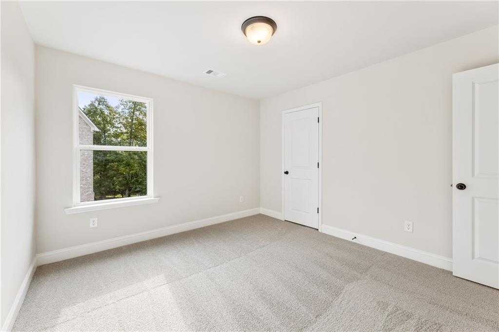 Bright secondary bedroom with white walls, beige carpet, and tree-view window in Davidson Homes The Hickory B, Buford, GA