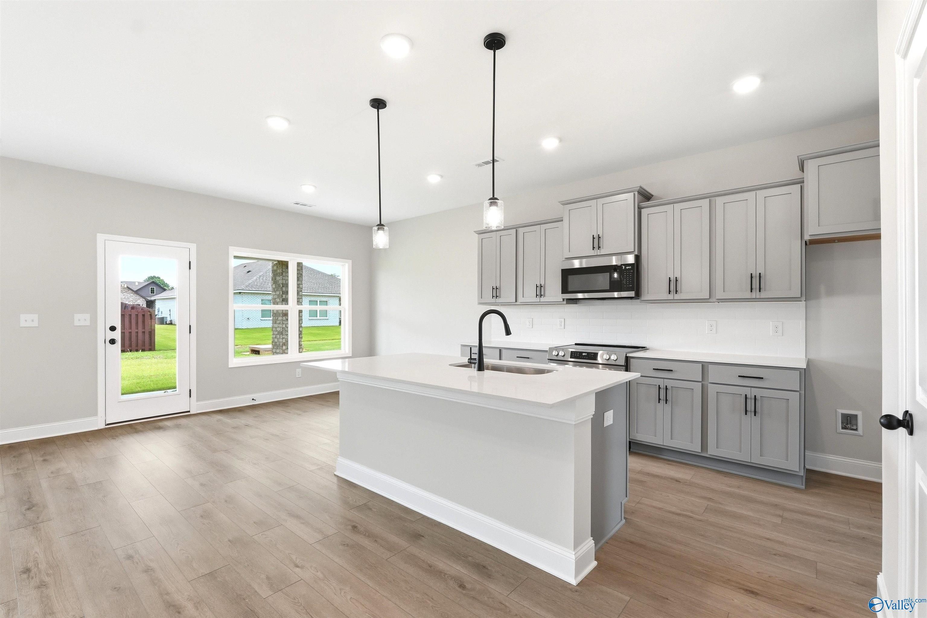 Modern kitchen with gray cabinets, quartz island, and pendant lighting in The Shelby A floor plan, Wood Trail, Toney, AL.