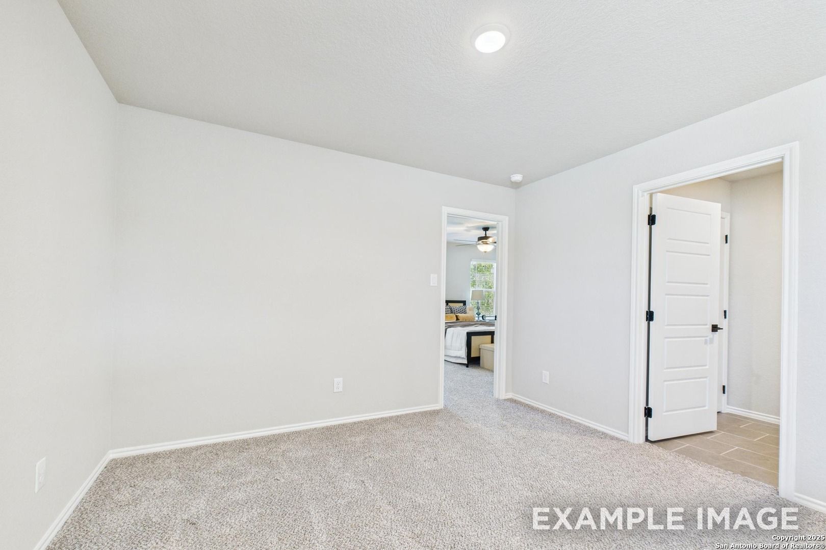Empty bedroom with white walls, carpet flooring, and open doorway to kitchen in Davidson Homes The Charlotte A, San Antonio