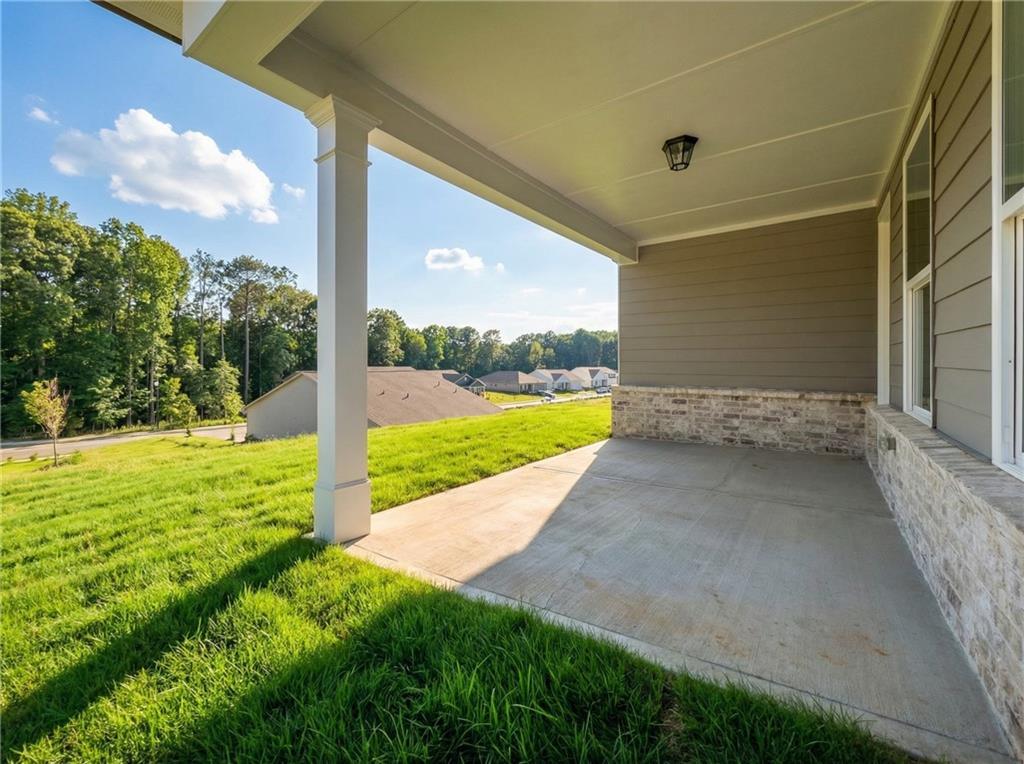 Covered porch with white columns, concrete flooring, and lush green yard view in Davidson Homes The Glenwood C, Kelly Preserve, Loganville, Georgia