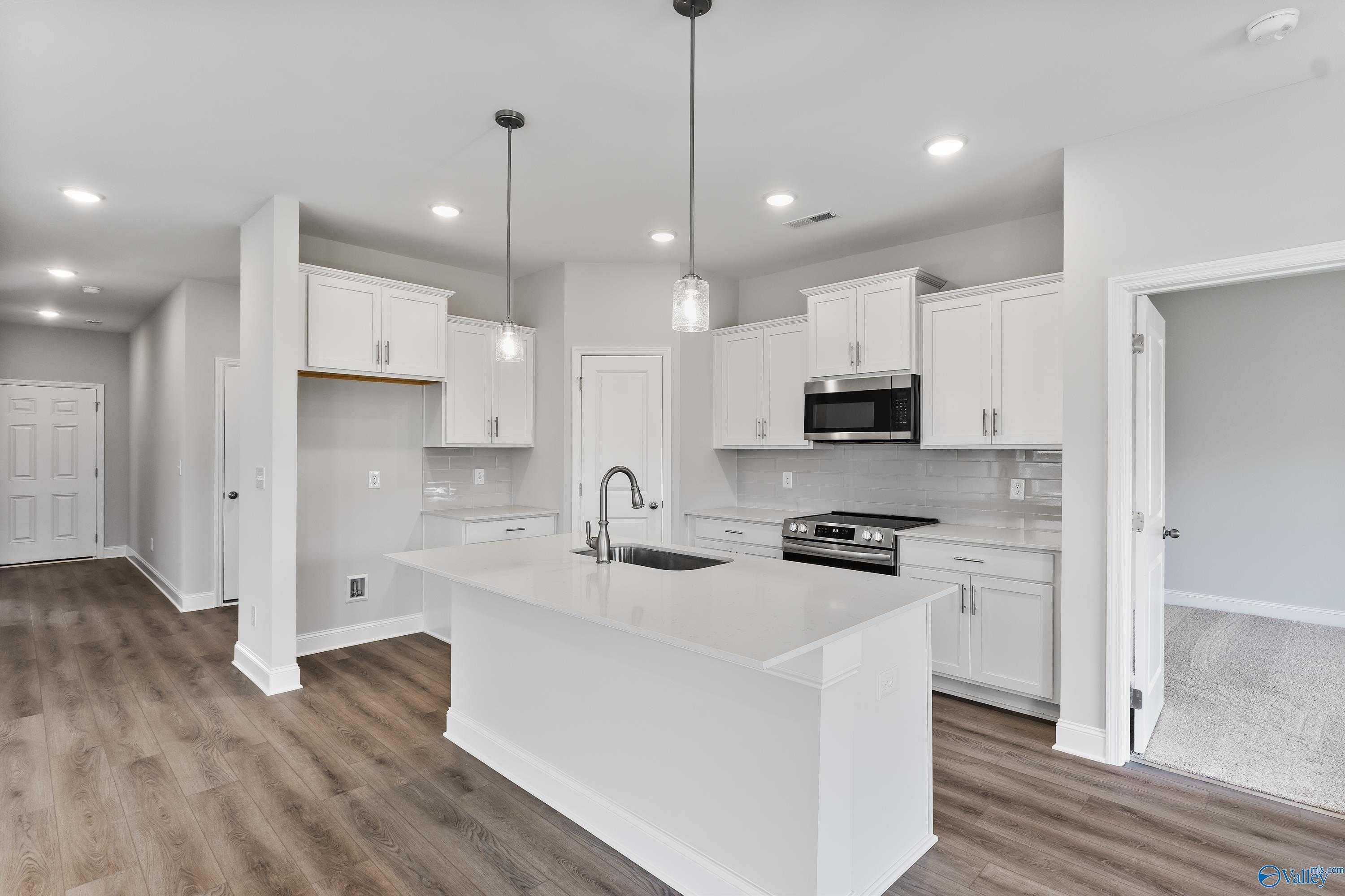 Modern white kitchen with large island sink, stainless appliances, pendant lights in Davidson Homes The Franklin C, Toney, Alabama
