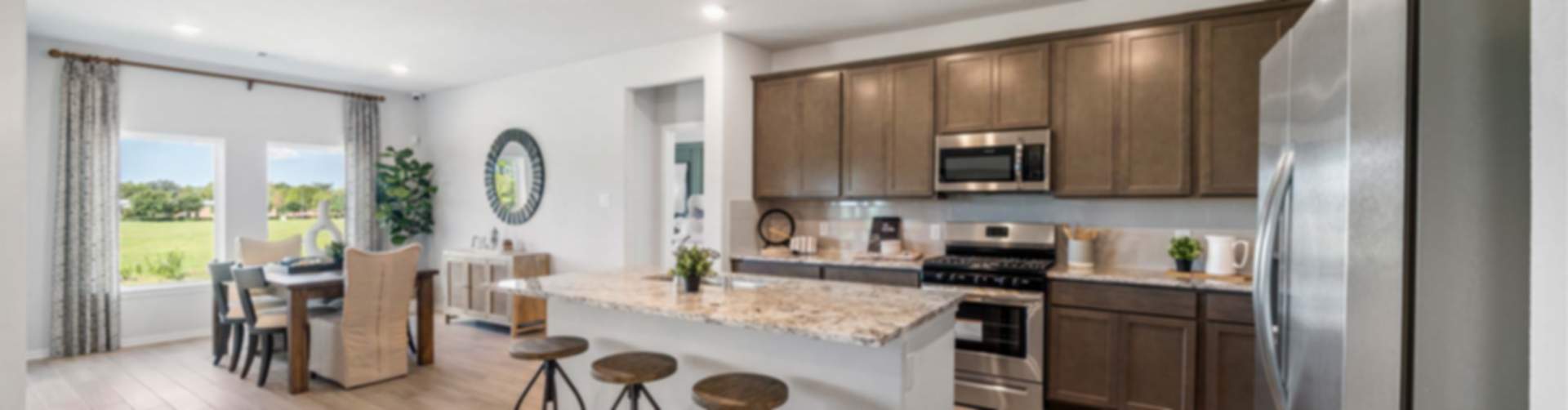 Modern open kitchen with granite island, bar stools, stainless appliances, and dining area in new Dayton home