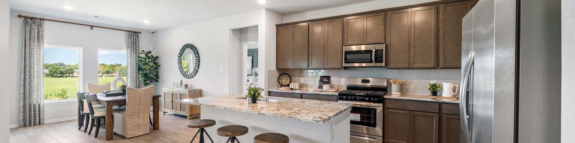 Modern open kitchen with granite island, bar stools, stainless appliances, and dining area in new Dayton home