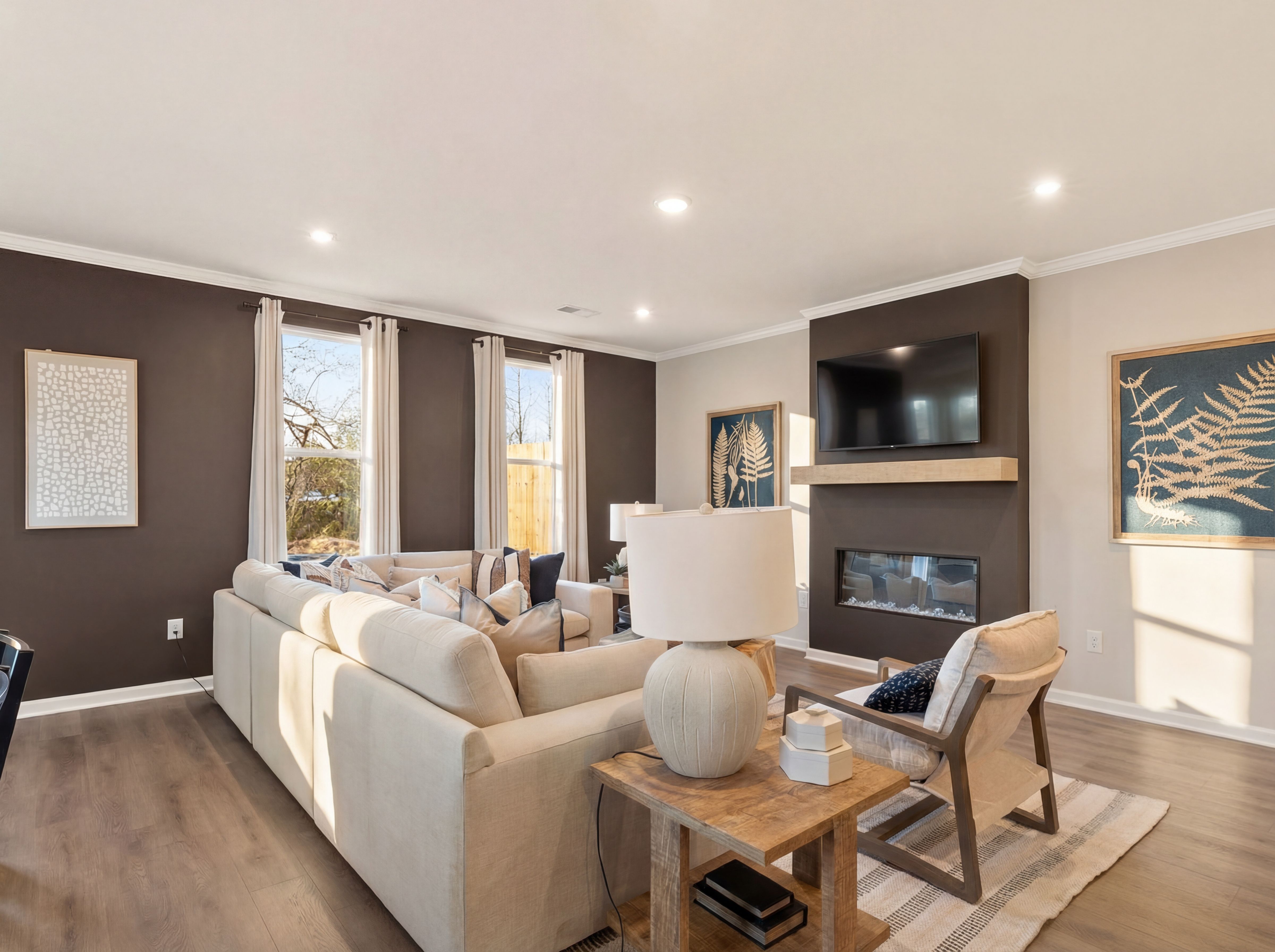 Cozy neutral living room in Lake Shore Winder GA with L-shaped sofa, gas fireplace, TV, and hardwood floors by Davidson Homes