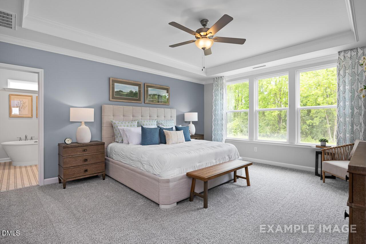 Bright primary bedroom with tray ceiling, ceiling fan, large windows, and tufted headboard in Davidson Homes Magnolia II B, Holly Springs NC