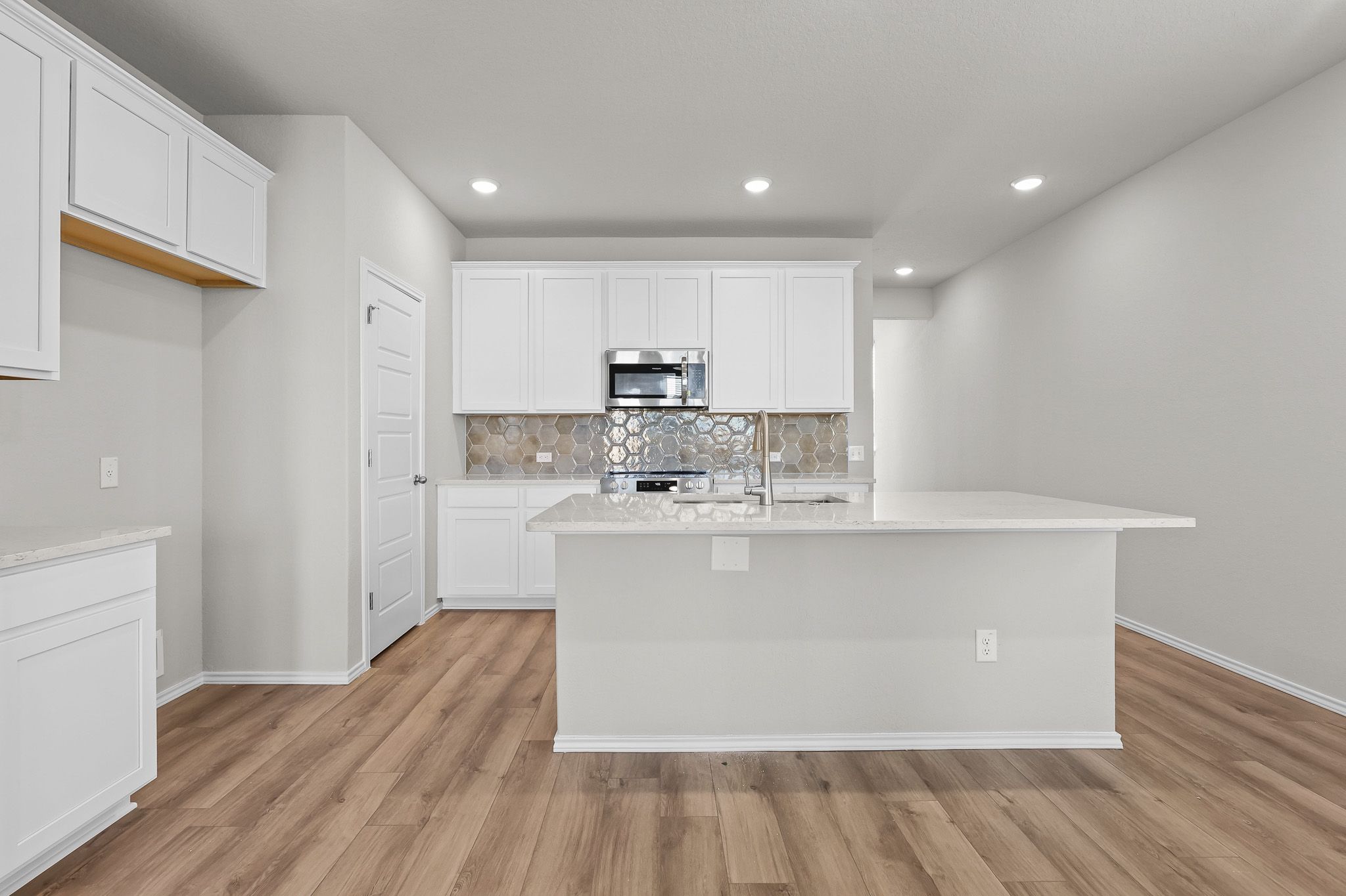 Modern kitchen in The Colorado B featuring white cabinets, stone backsplash, and a spacious island in San Antonio, Texas.