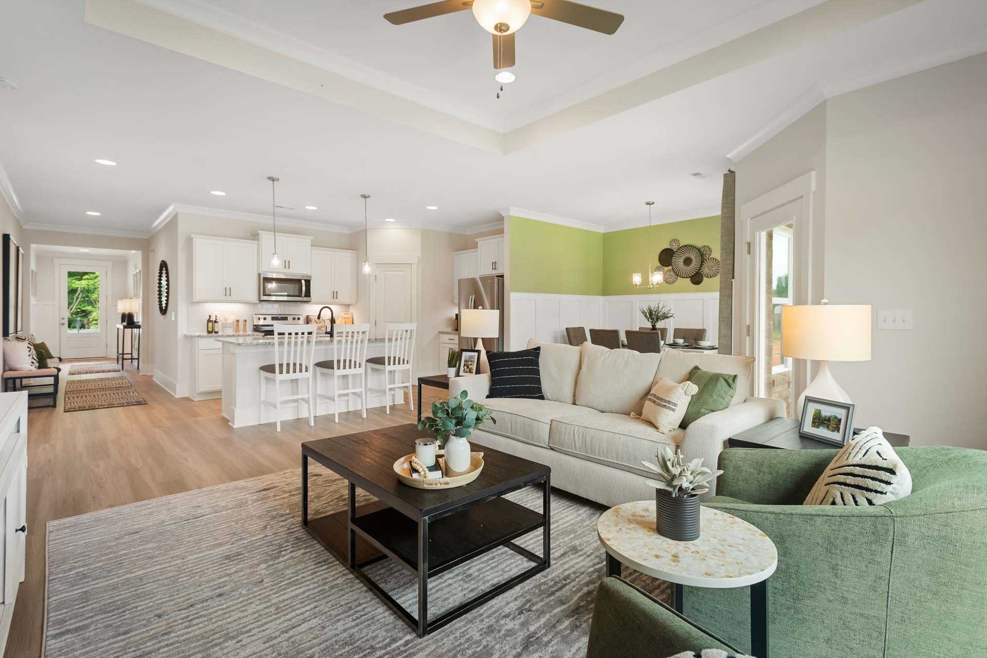 Open-concept kitchen and living room in Durham Farms, Harvest AL featuring white cabinets, island, green accent wall, hardwood floors