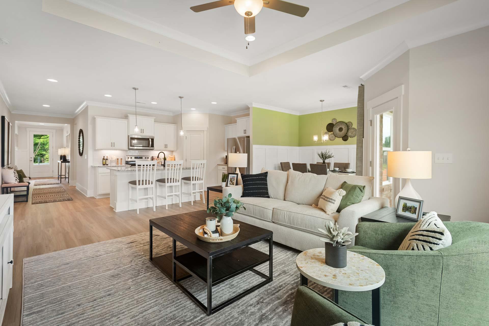 Open-concept kitchen and living room in Durham Farms, Harvest AL featuring white cabinets, island, green accent wall, hardwood floors