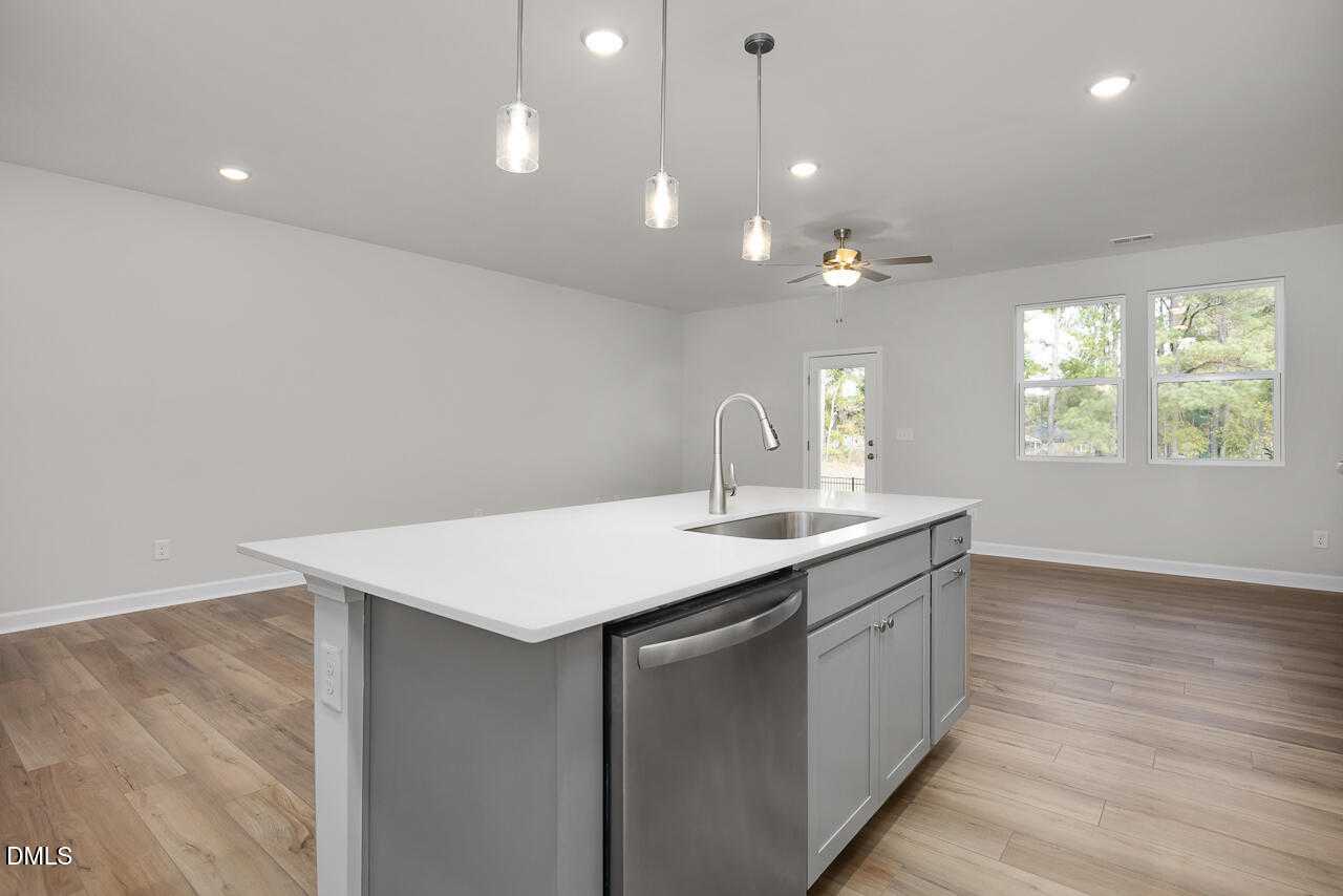 Modern open-concept kitchen with white island, stainless dishwasher, pendant lights, and ceiling fan in Davidson Homes The Warren, Fuquay-Varina, NC