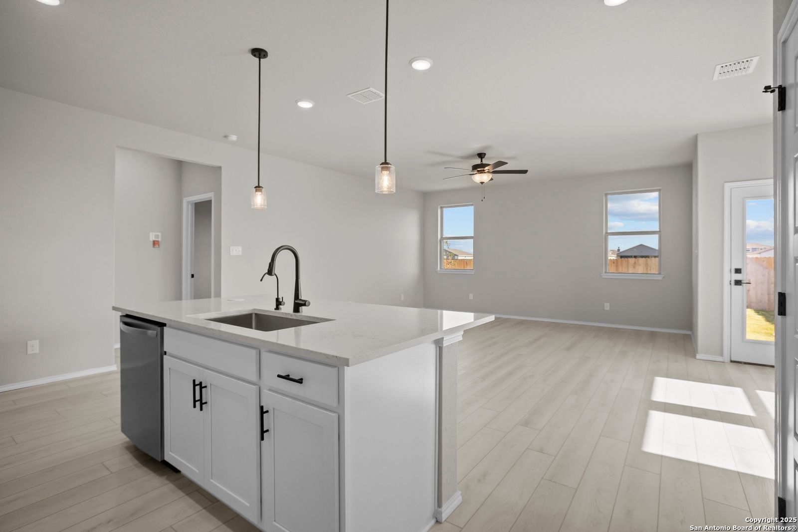 Modern white kitchen island with farmhouse sink, pendant lights, and ceiling fan in open-concept living space of The Daphne H, Seguin, TX