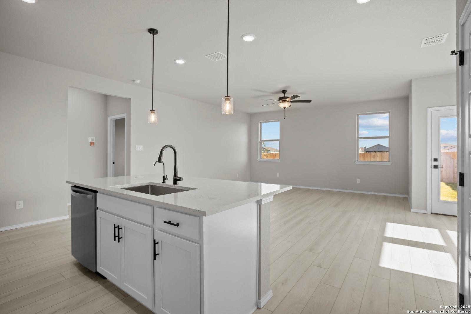 Modern white kitchen island with farmhouse sink, pendant lights, and ceiling fan in open-concept living space of The Daphne H, Seguin, TX