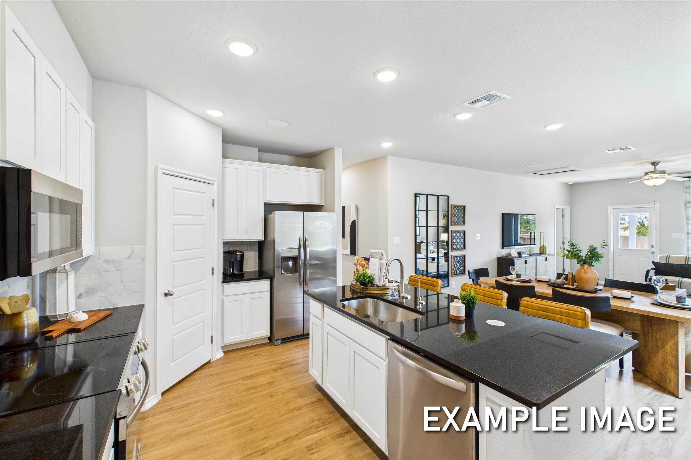 Modern open-concept kitchen with white cabinets, black granite island, stainless appliances, and adjacent dining in The Sabine C, San Antonio