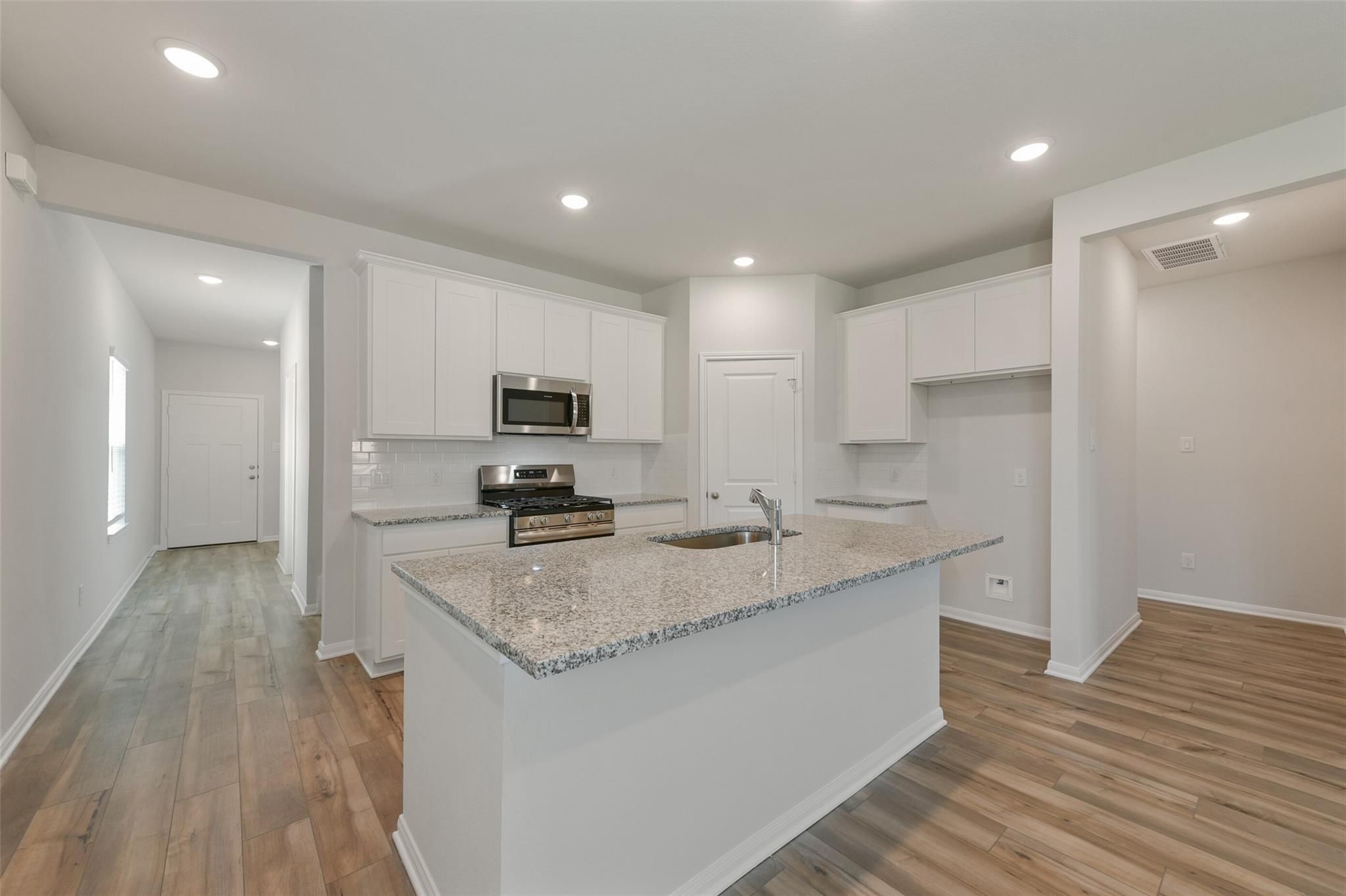 Modern white kitchen with granite island sink, stainless appliances, open layout in Davidson Homes The Sabine F, Dayton, Texas